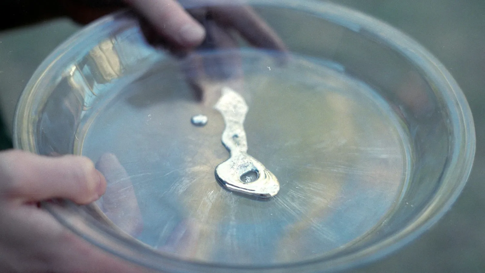 A bead of shiny liquid in a shallow glass dish held in a hand