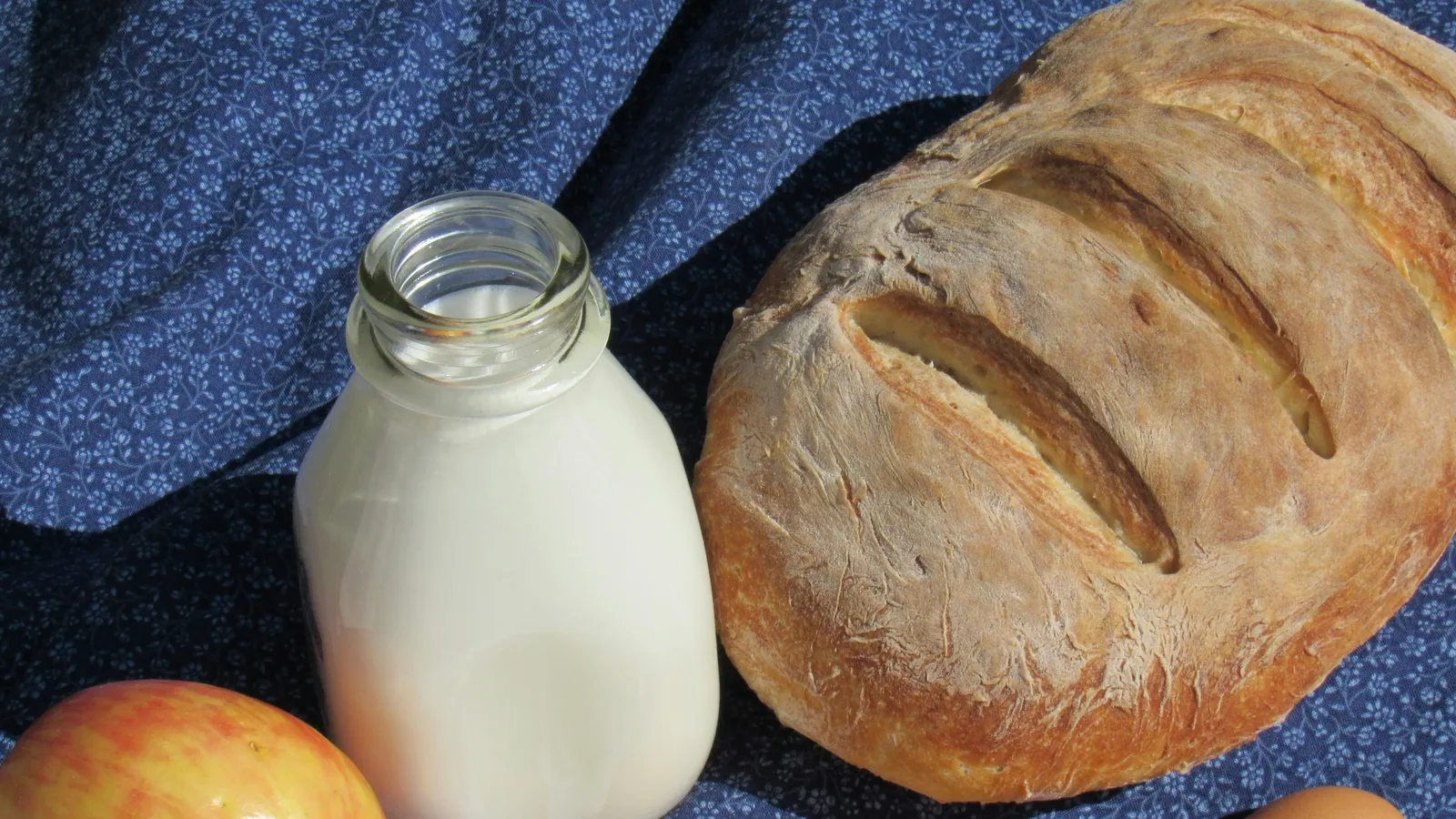 A bottle of milk, bread, cheese and eggs on a table