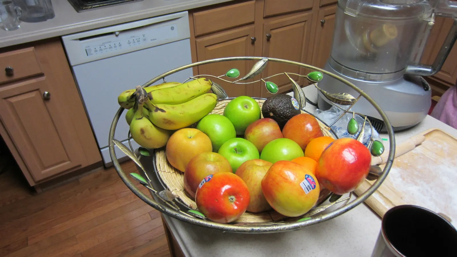 A bowl of bananas, apples and tomatoes on a kitchen counter