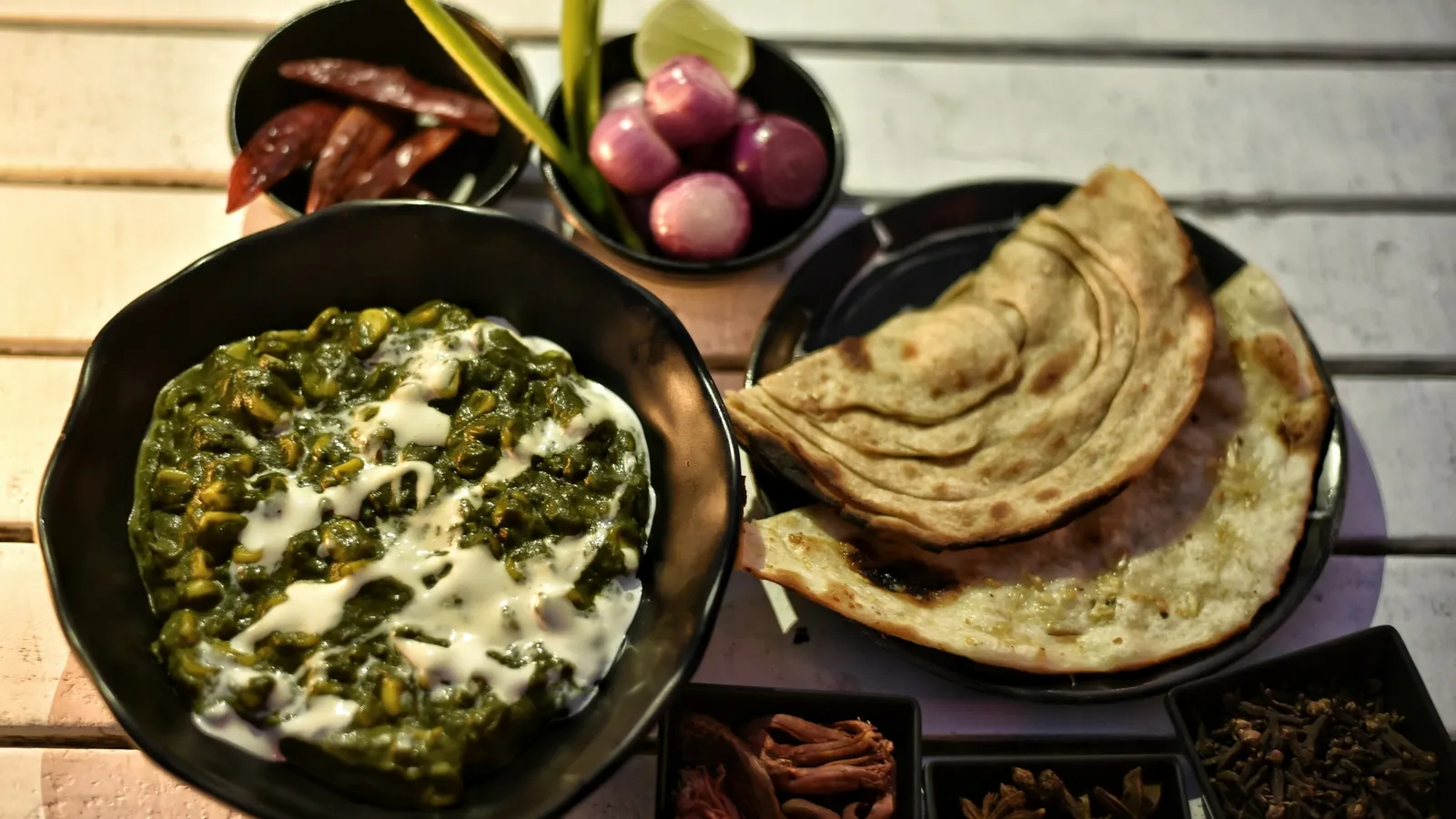 A bowl of spinach curry served with flatbread and onions