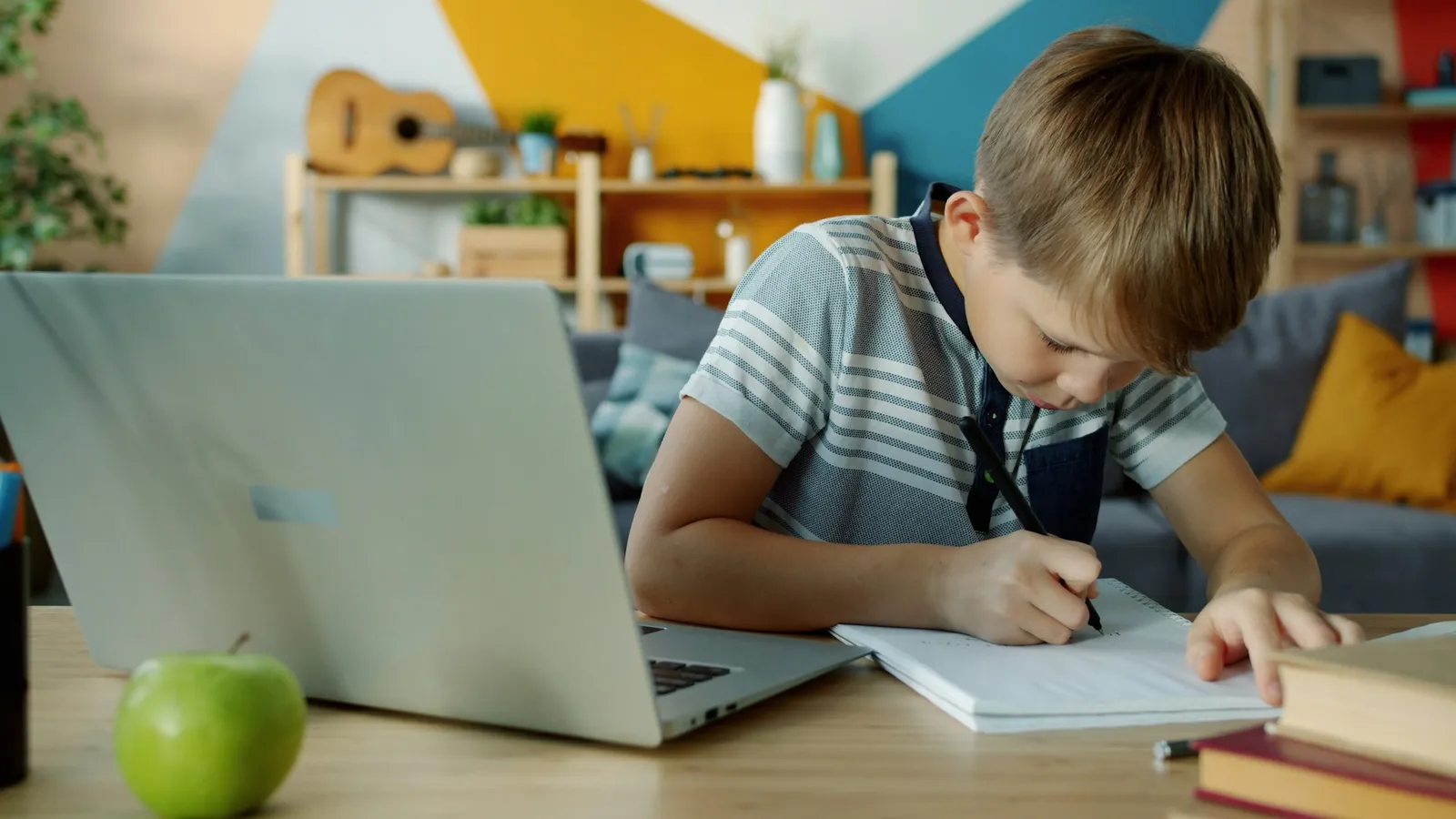 A boy studying at a laptop with a notebook at home