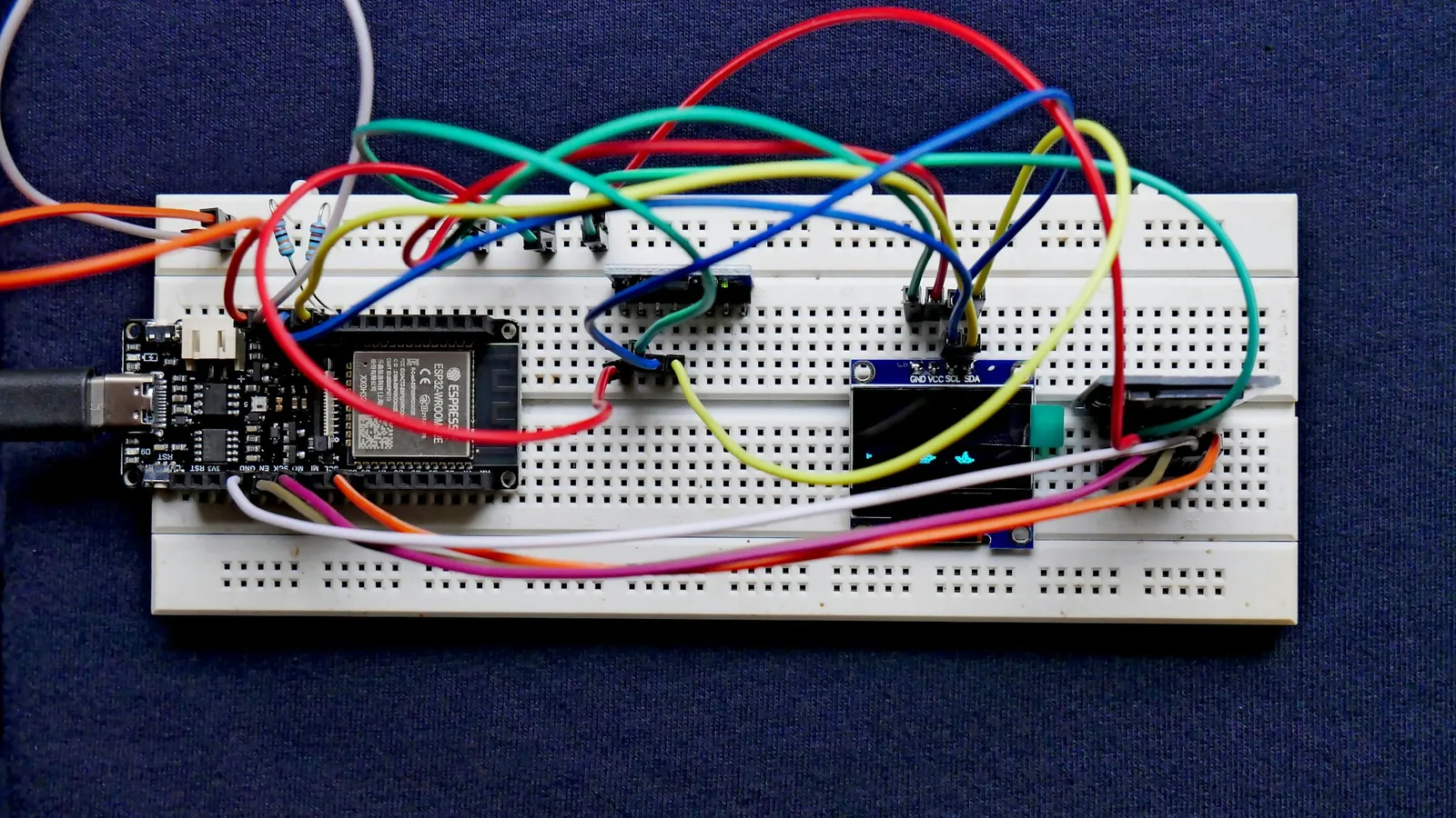 A breadboard circuit with coloured jumper wires on a dark blue surface