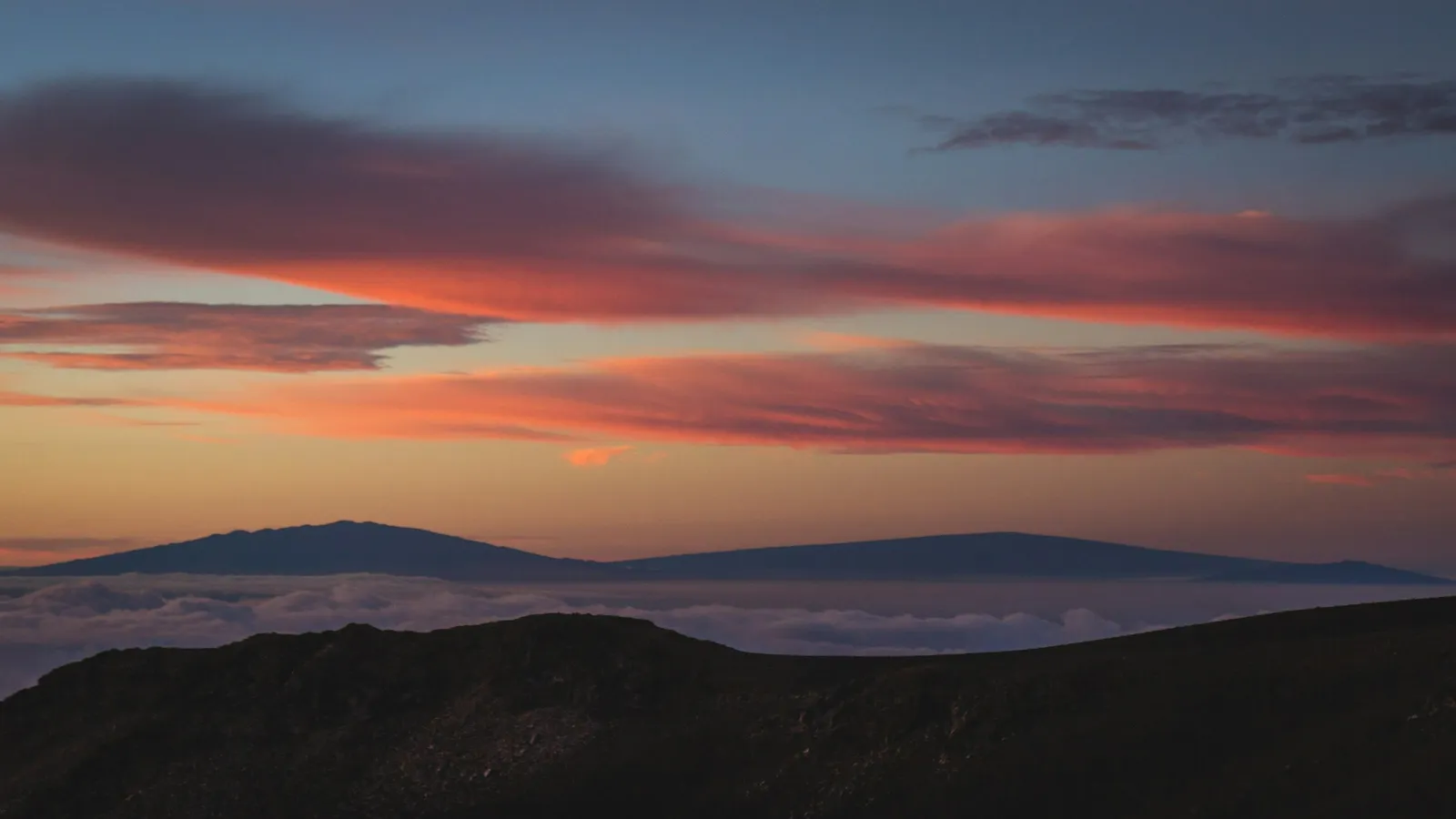 A broad volcano silhouetted under a red sunset sky