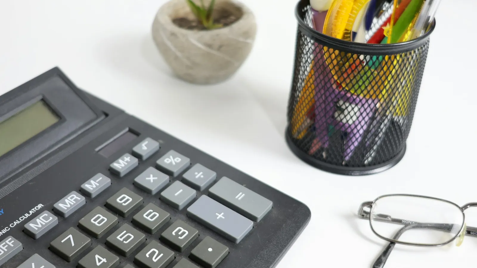 A calculator, glasses and pens on a desk