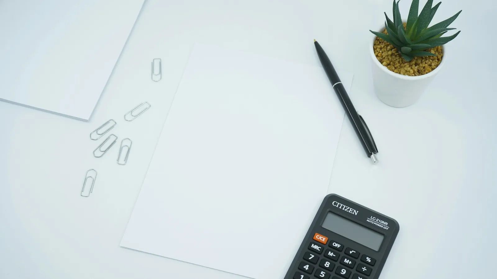 A calculator, pen and paper on a white desk
