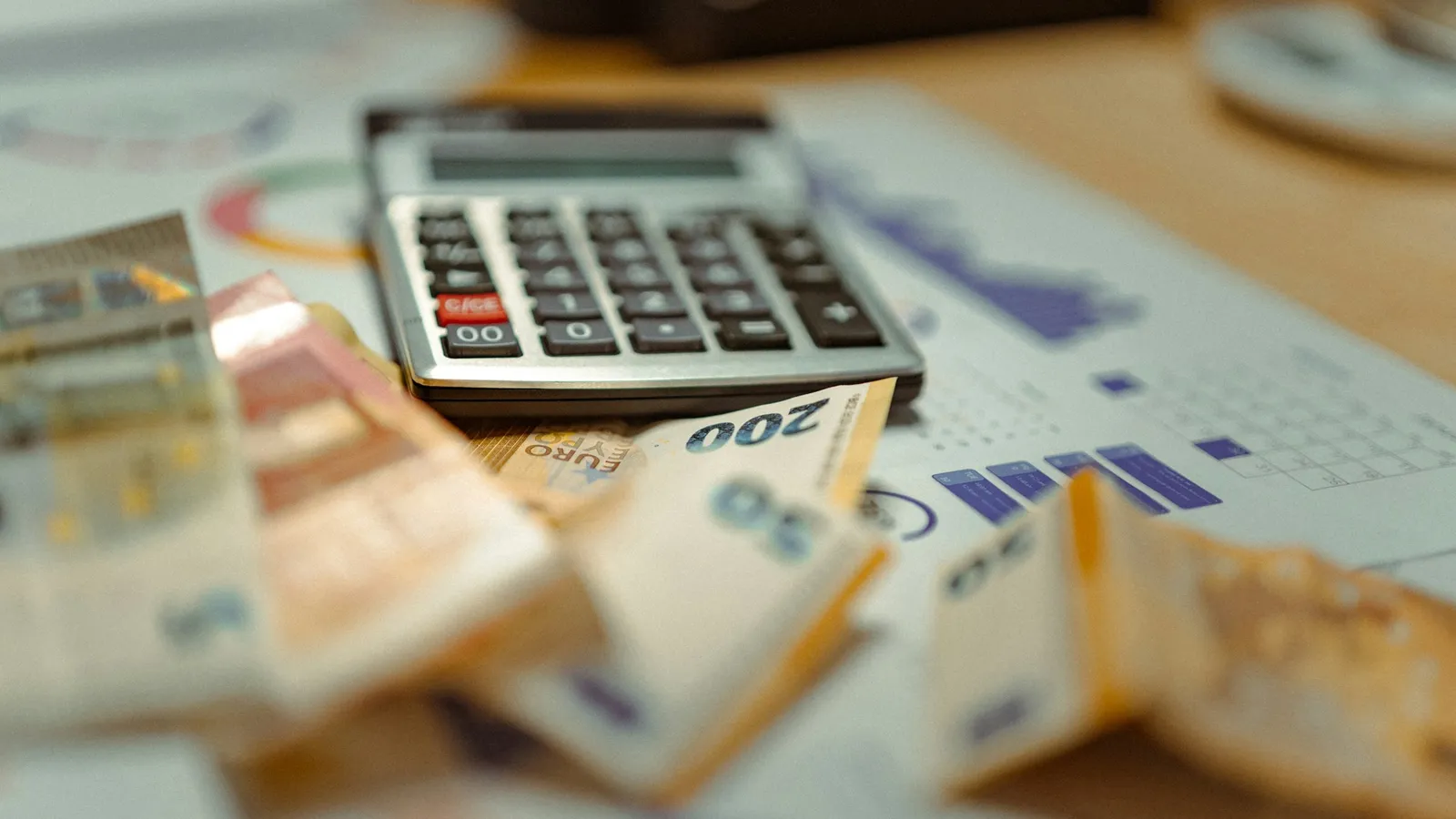 A calculator resting on banknotes beside printed charts