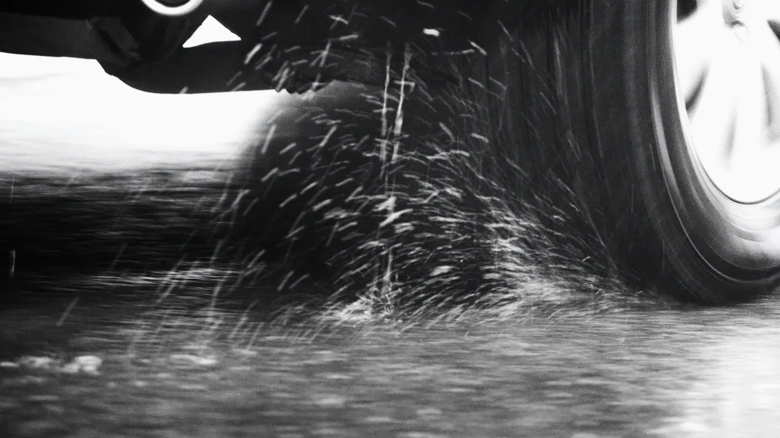 A car tyre throwing up spray on a wet road, in black and white