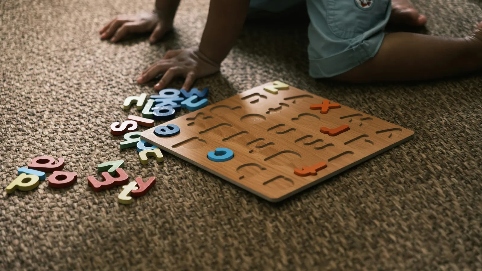A child fitting pieces into a wooden alphabet puzzle on a carpet