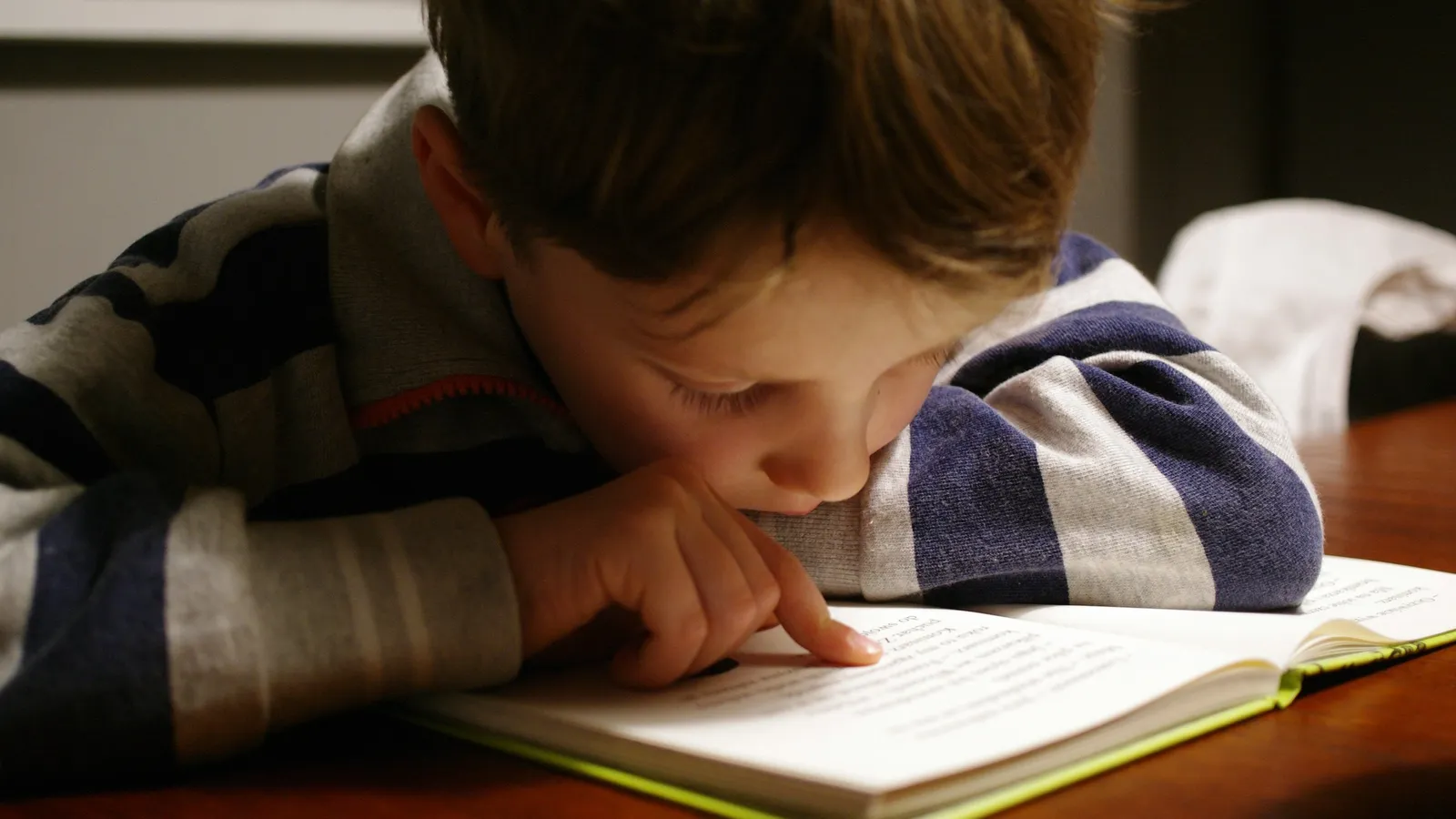 A child leaning close over an open book at a wooden table