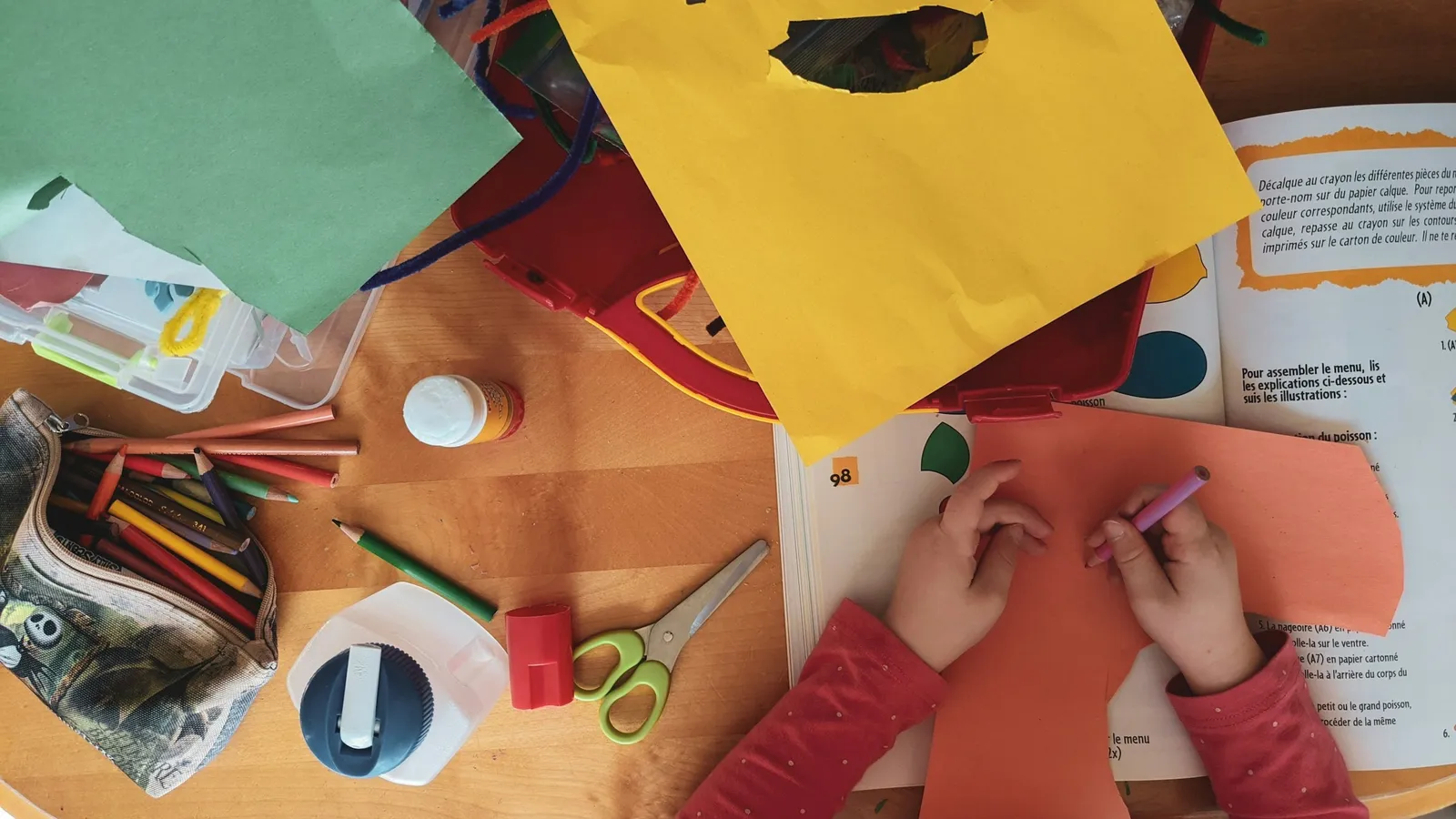 A child making a paper craft at a table covered in supplies