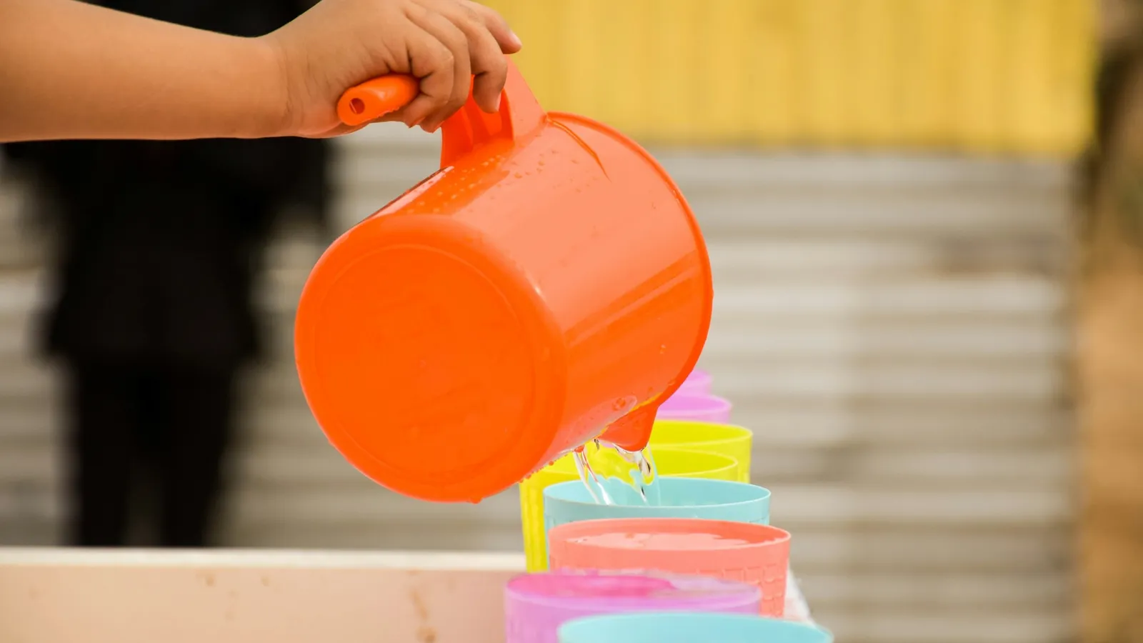 A child pouring water from an orange jug into a container