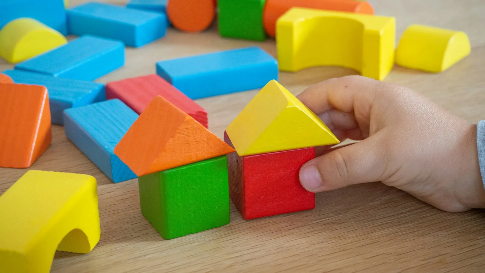 A child's hand arranging colourful wooden building blocks