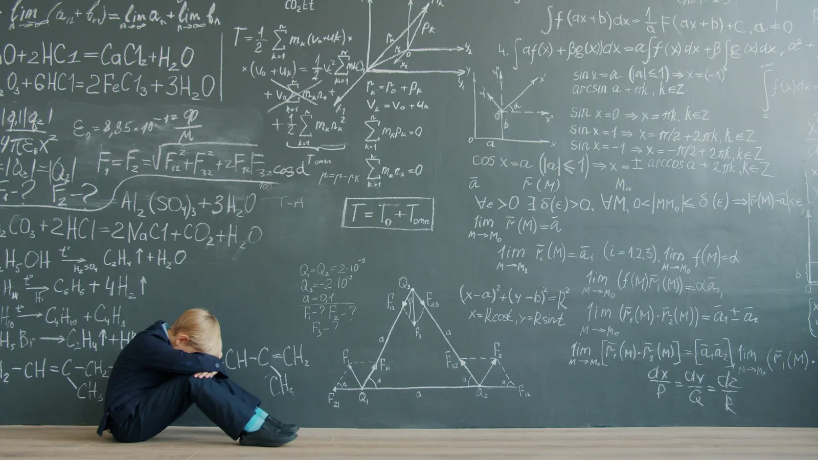 A child sitting below a chalkboard full of maths, head down