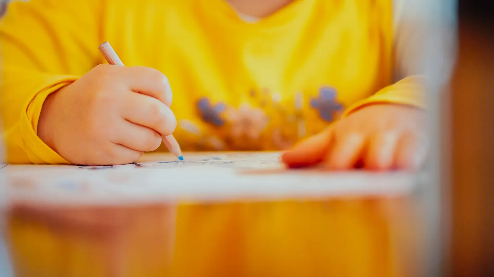 A child writing at a desk in yellow light