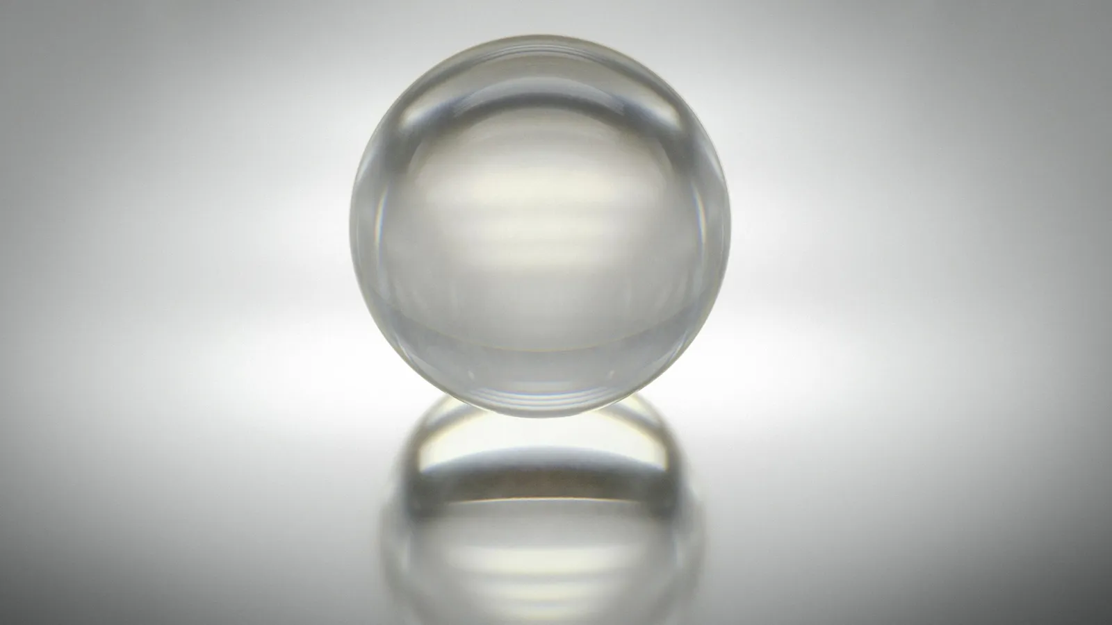 A clear glass sphere and its reflection on a white surface