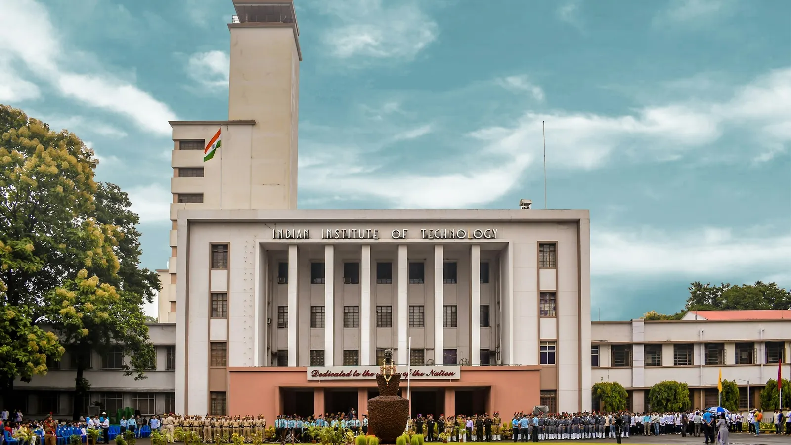 A college main building with a tall tower behind a green lawn