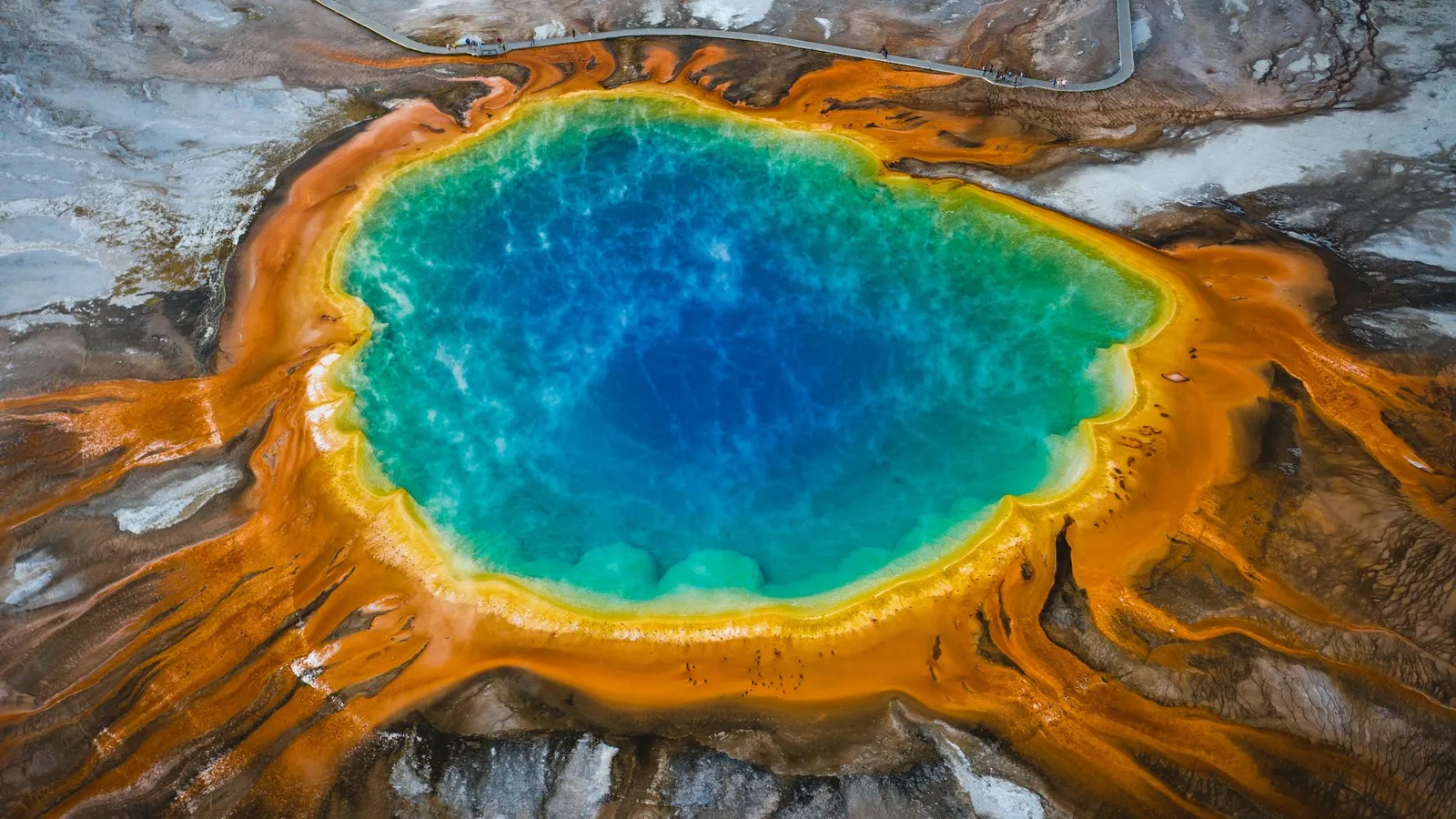 A colourful hot spring ringed with orange microbial mats, seen from above