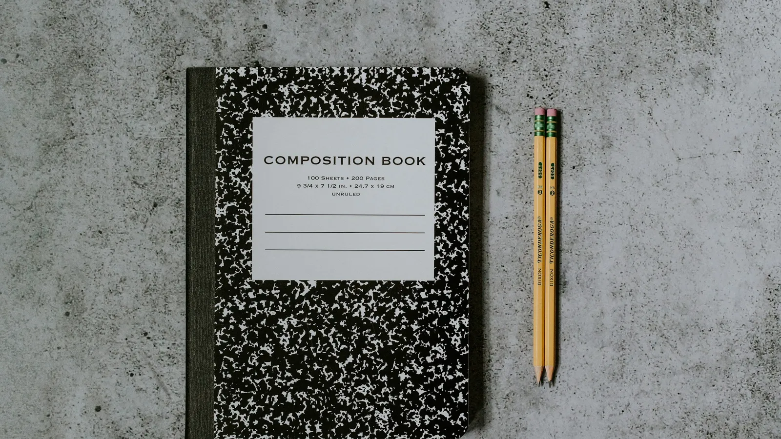 A composition notebook and pencil on a grey surface