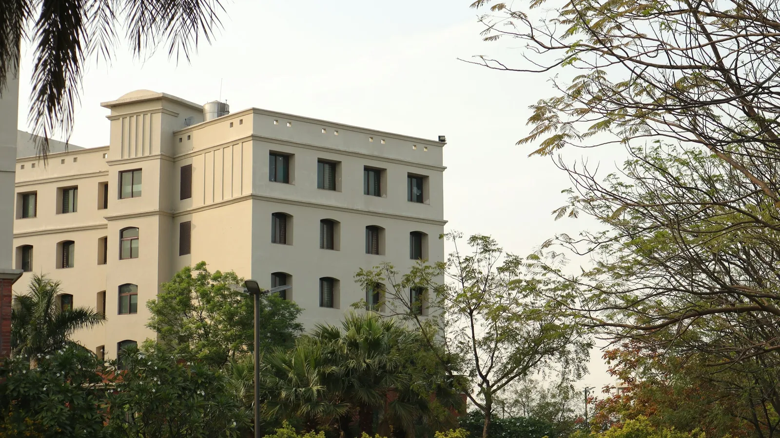 A cream college building framed by trees under a pale sky