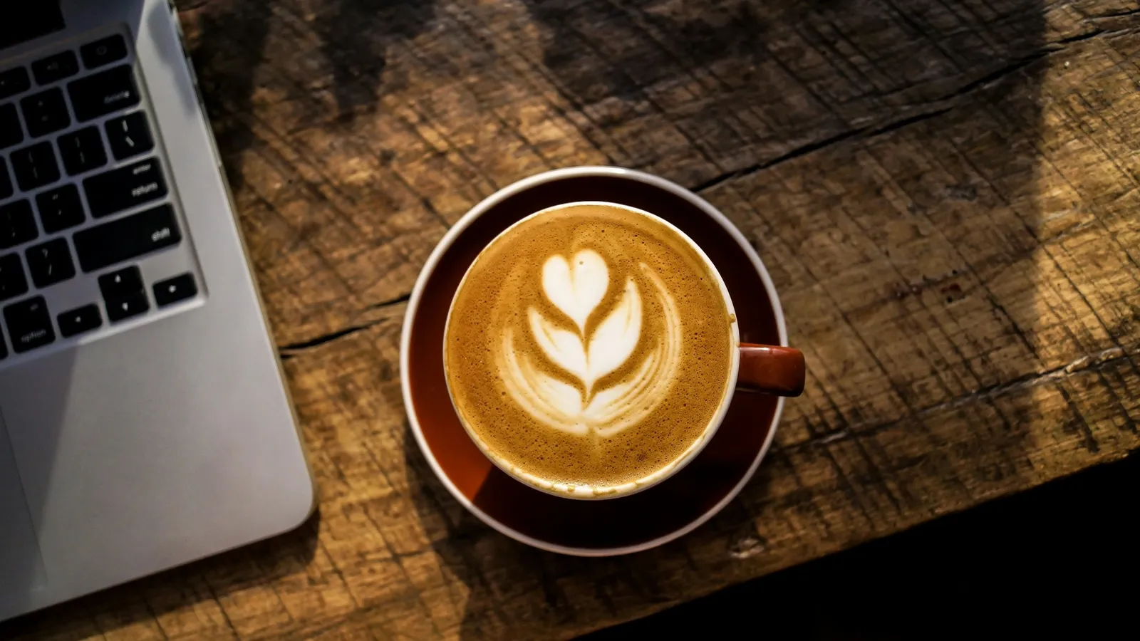 A cup of coffee beside a laptop on a wooden table