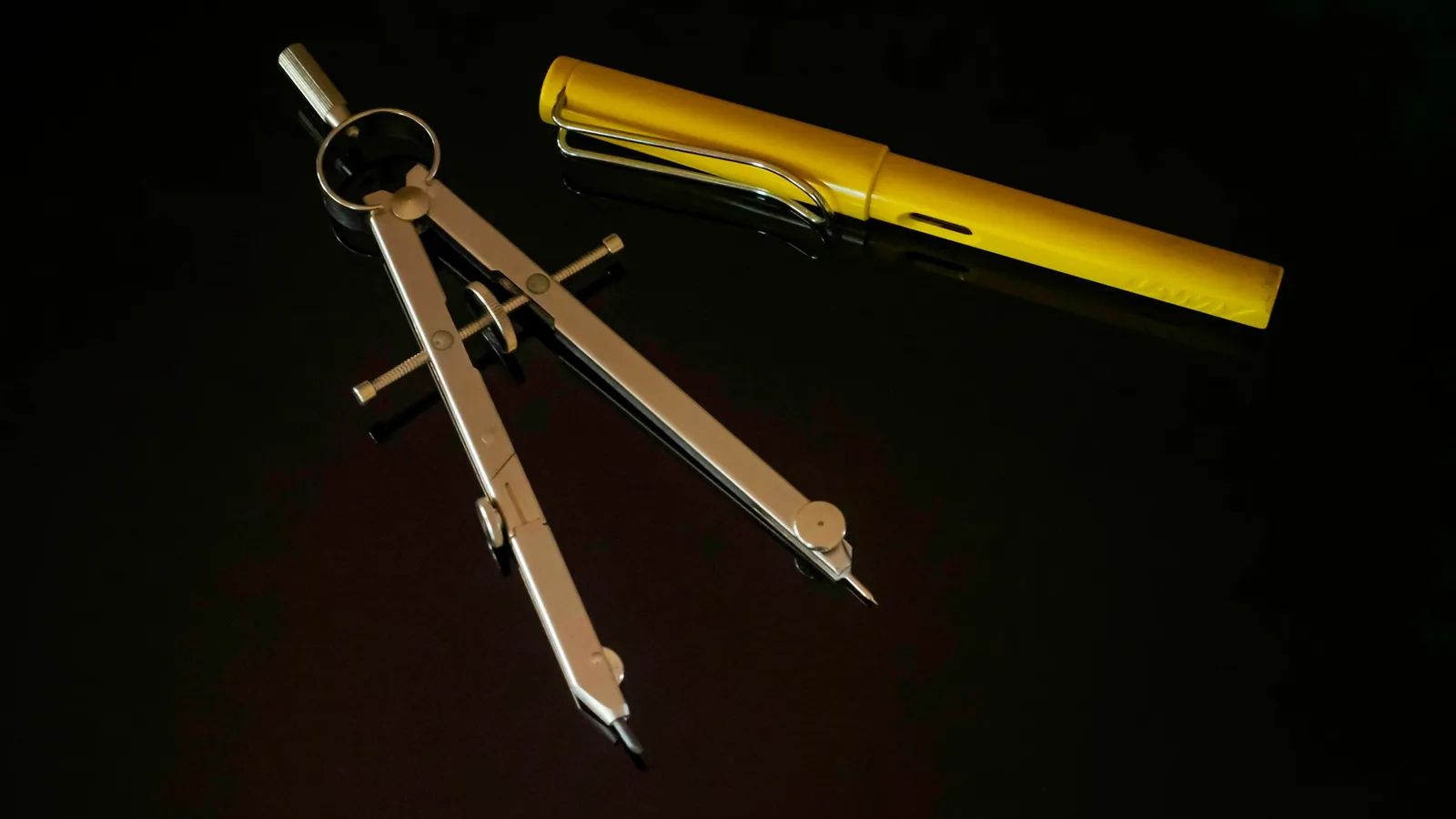 A drawing compass beside a yellow pencil
