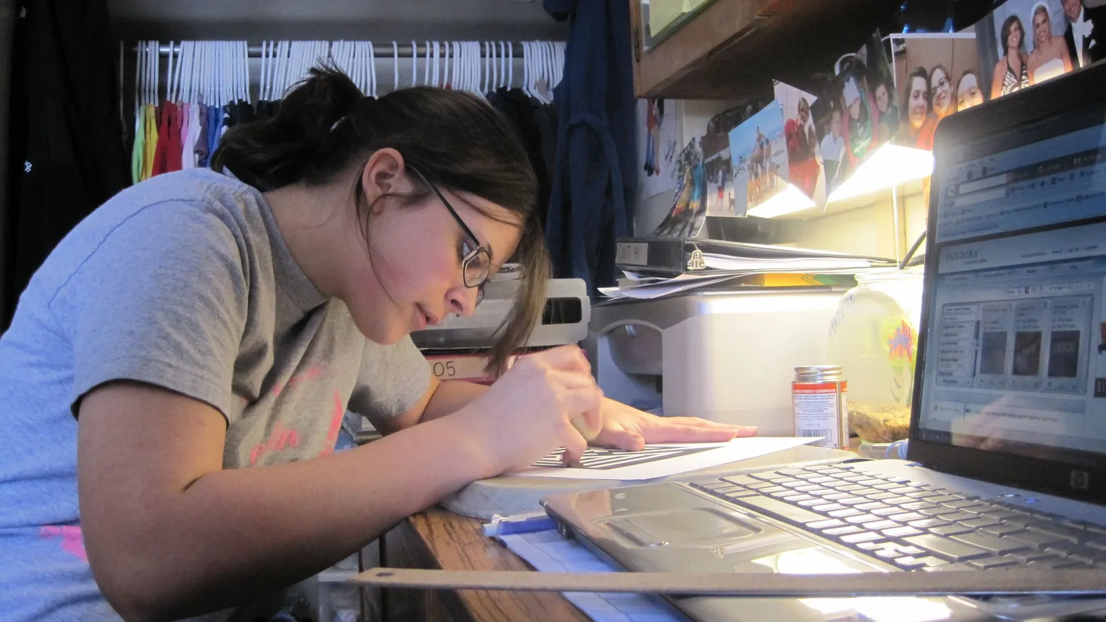 A female student writing and studying at a desk in a dorm room