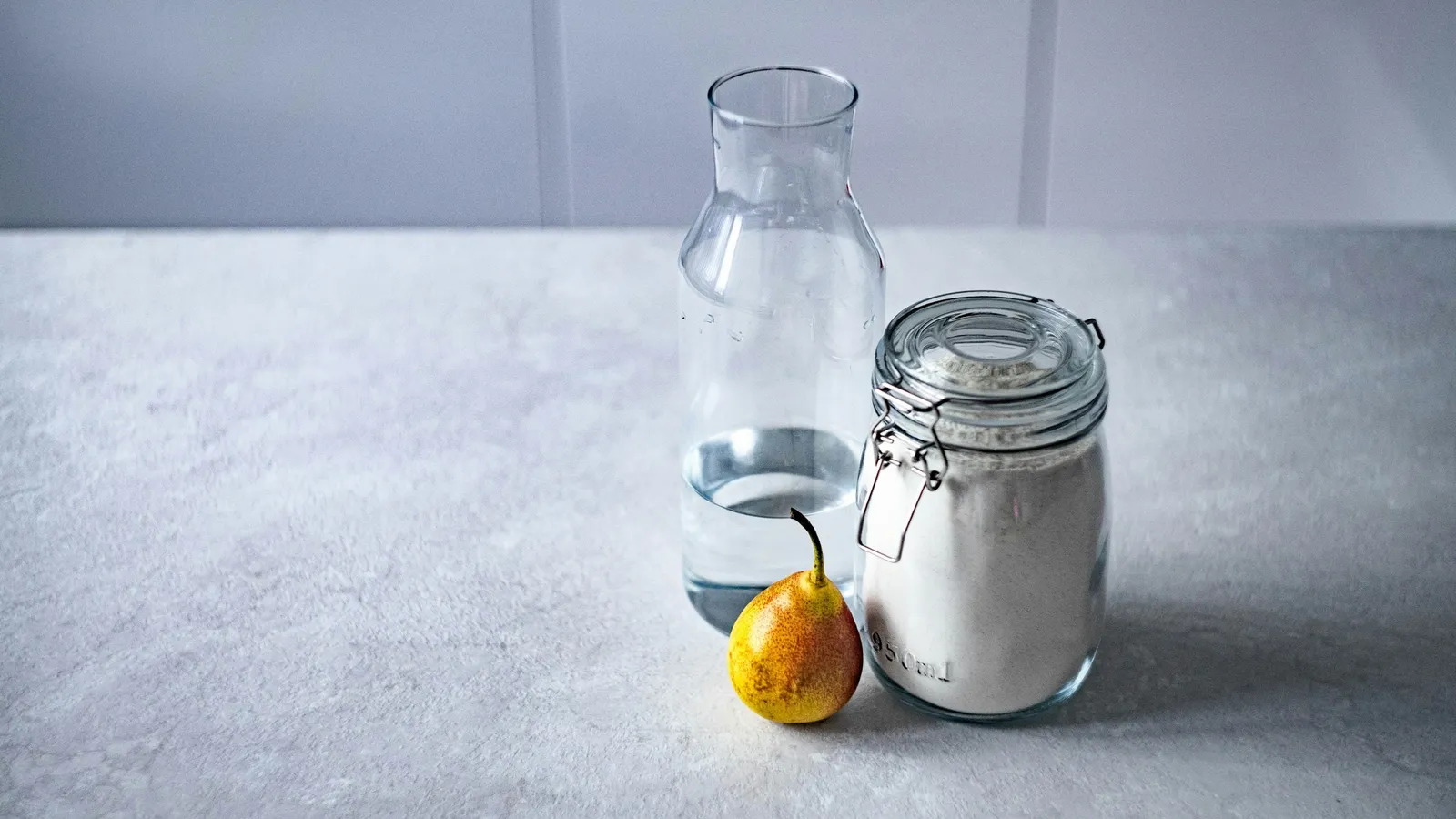 A glass bottle, a jar of white powder and a lemon on a kitchen counter