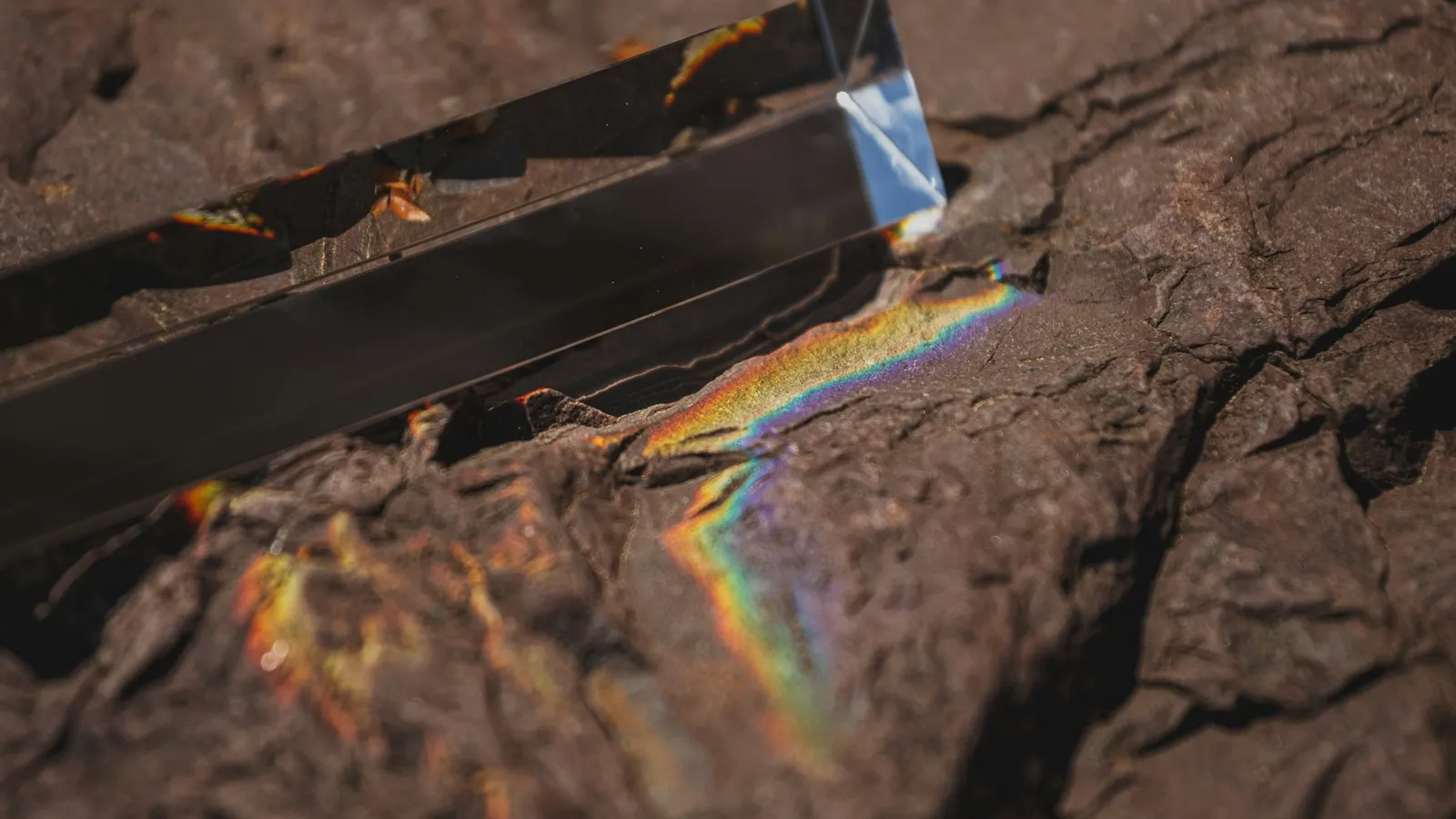 A glass prism casting a small rainbow onto a sandy surface
