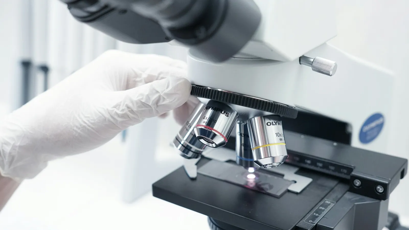 A gloved hand adjusting a microscope