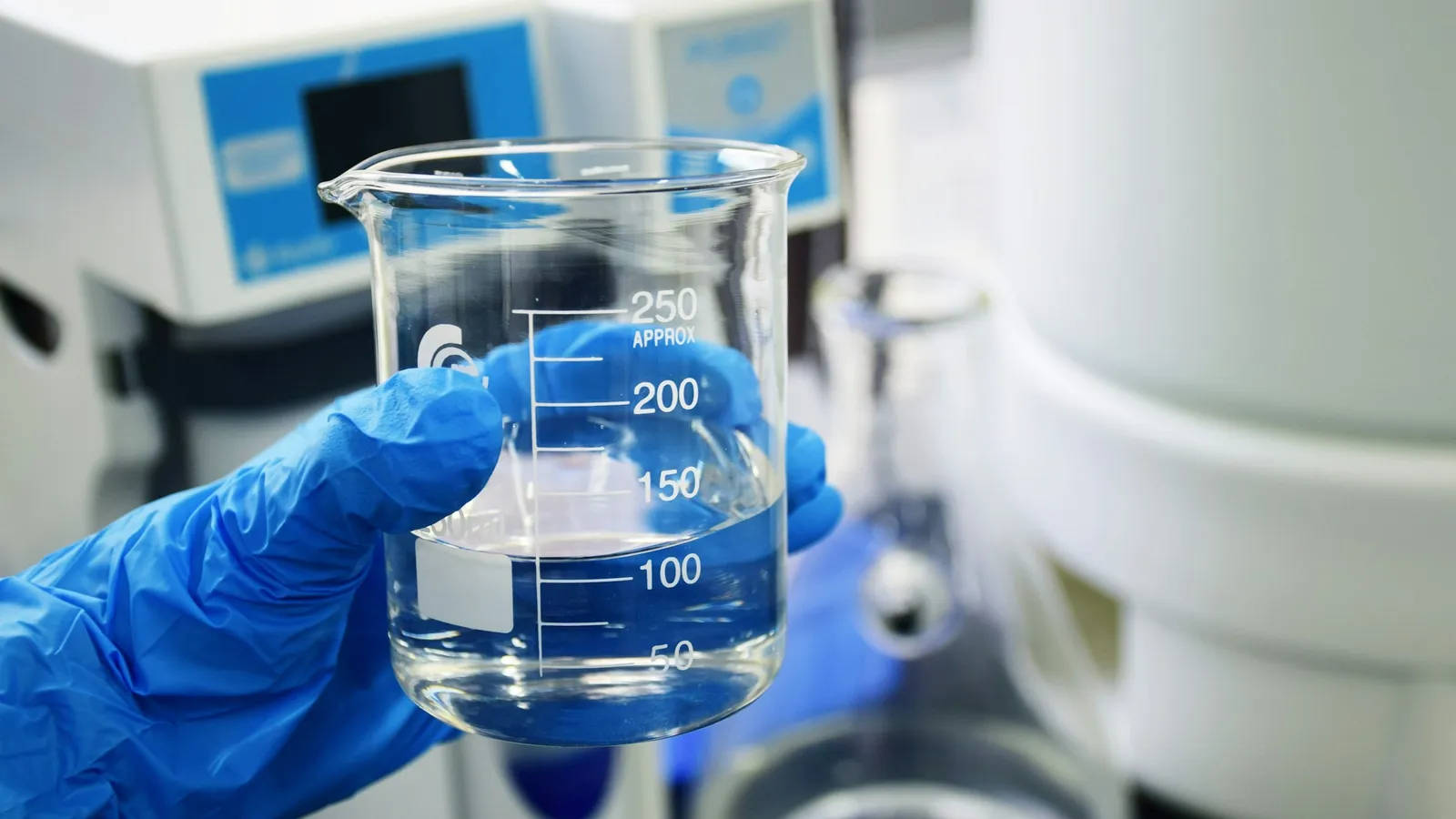 A gloved hand holding a beaker of clear liquid in a lab
