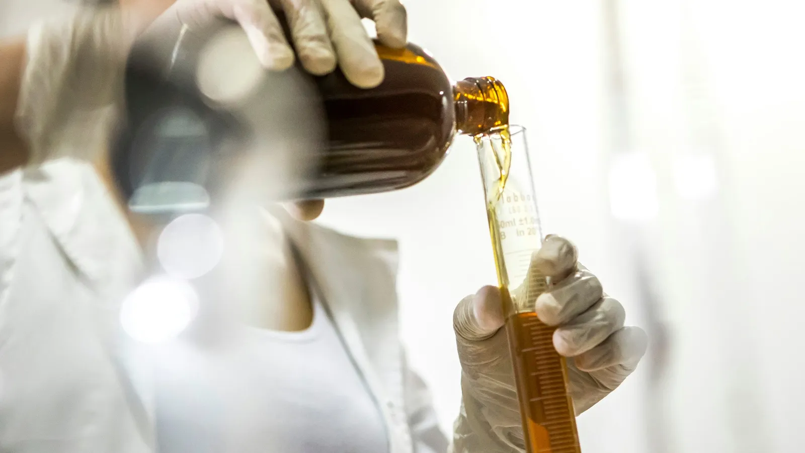 A gloved hand pouring an amber liquid in a lab