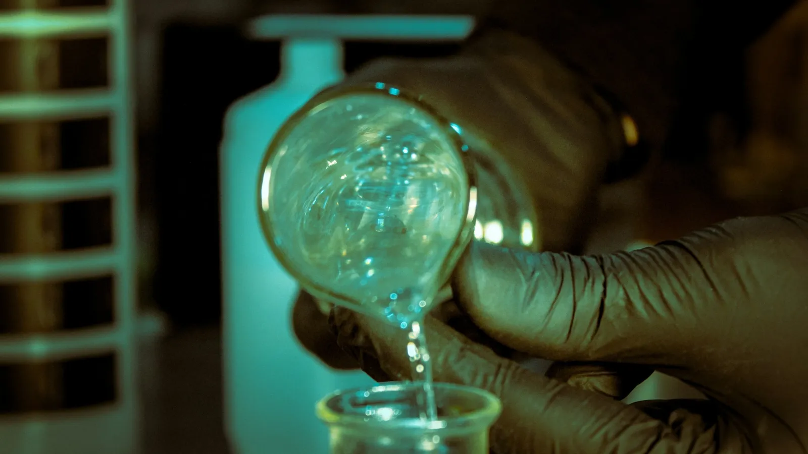 A gloved hand pouring liquid from a round flask