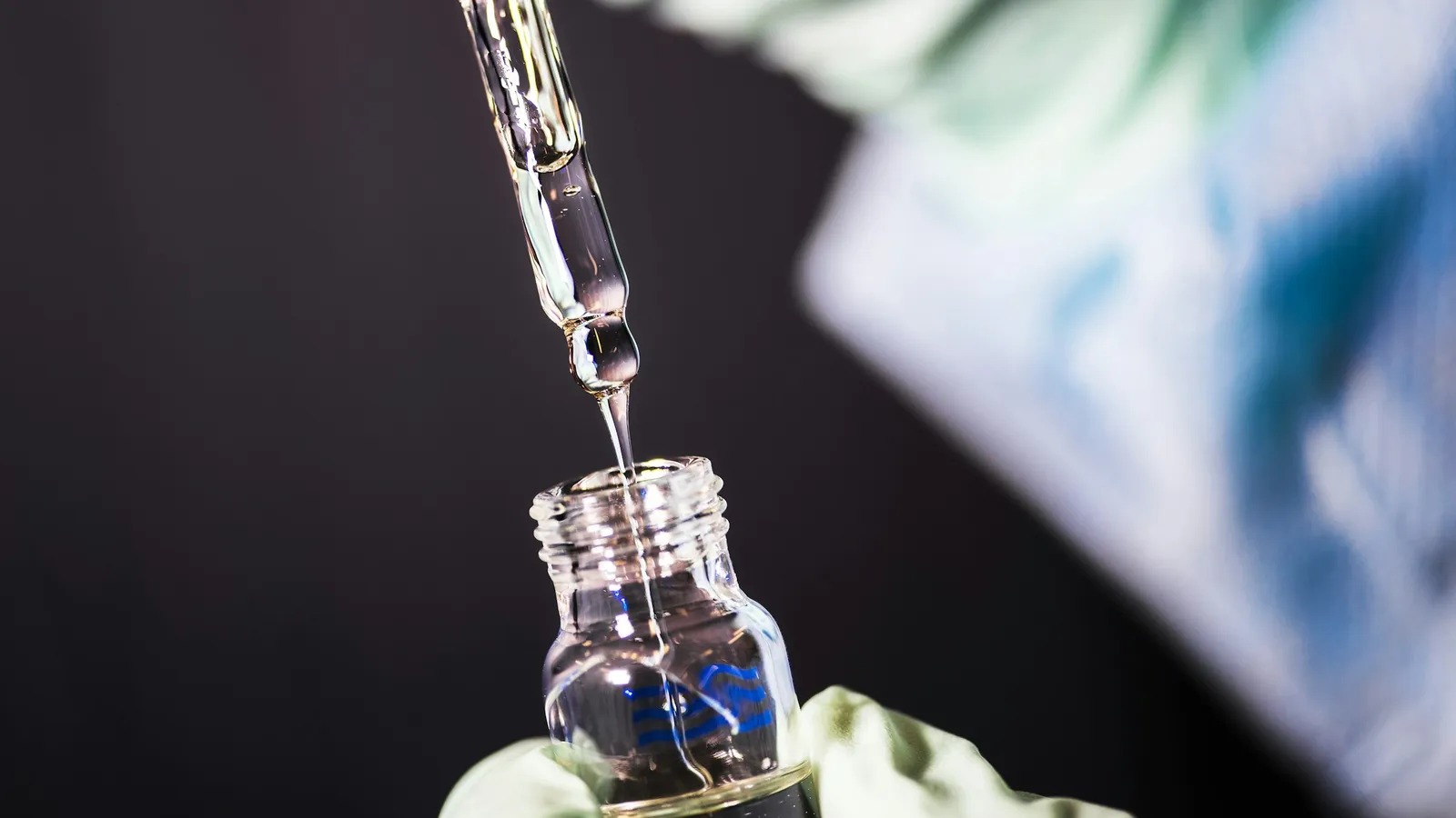 A gloved hand using a dropper over a small bottle