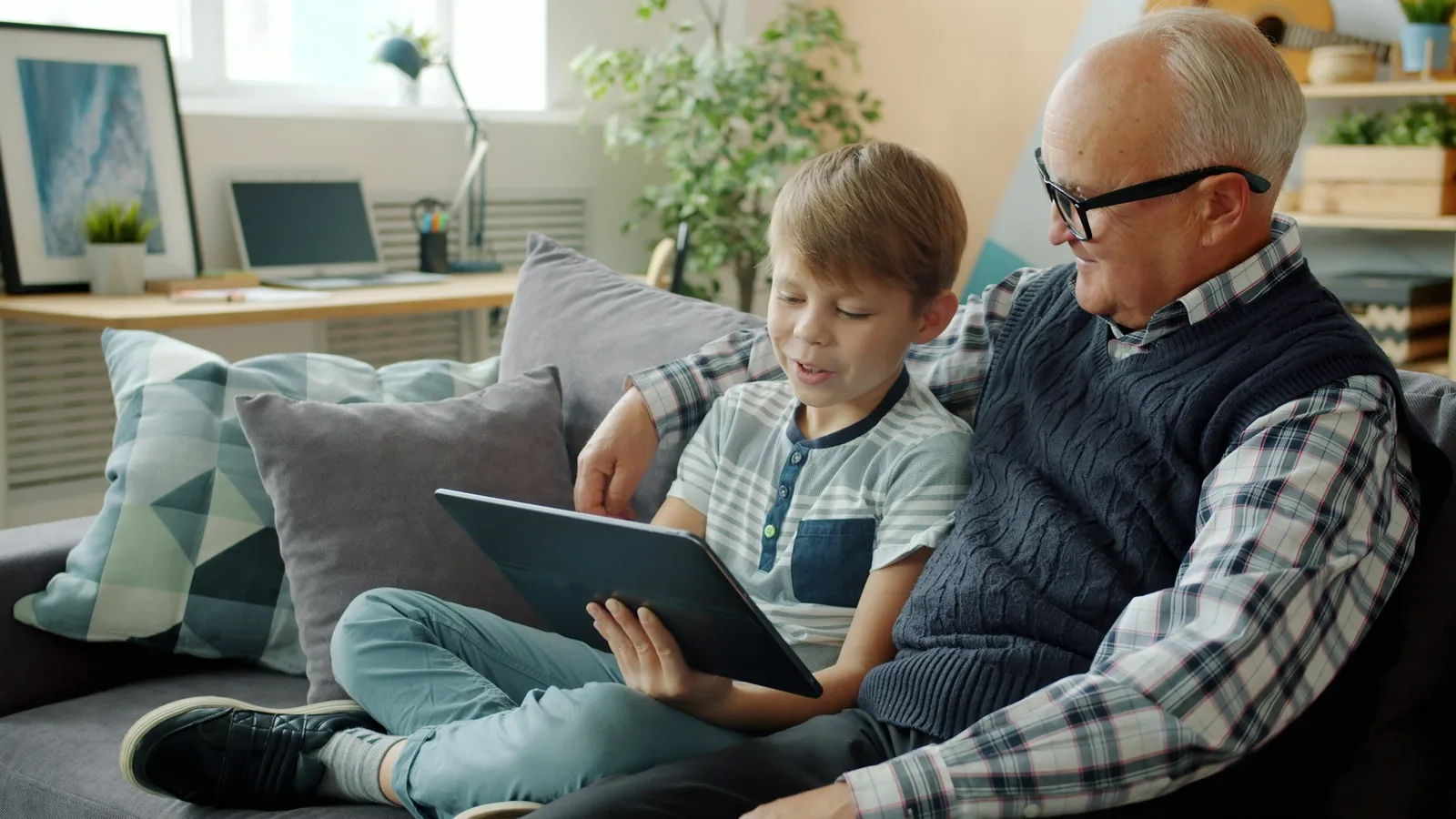 A grandfather and grandson looking at a tablet on a sofa