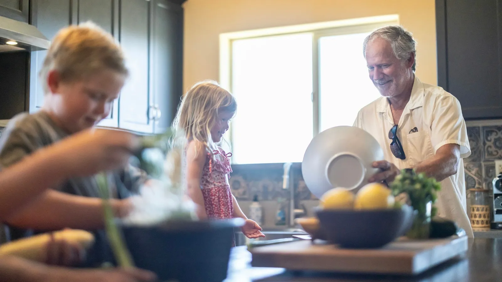A grandfather and two grandchildren preparing food together in a kitchen