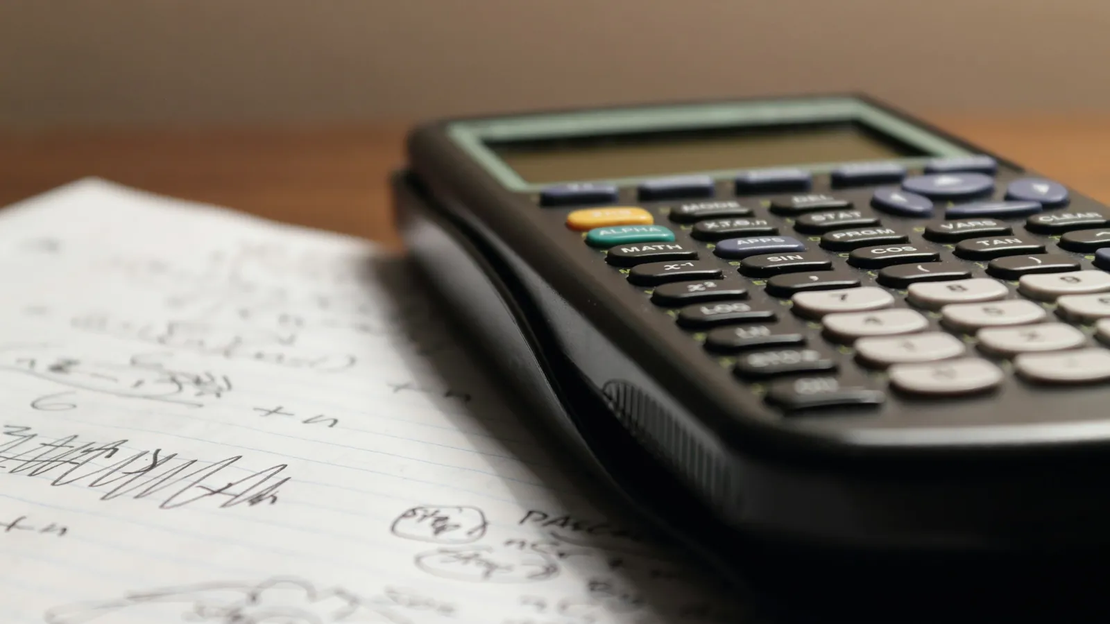 A graphing calculator resting on pages of handwritten maths