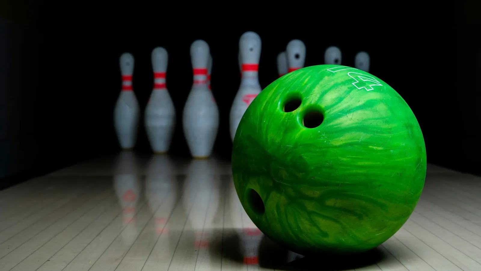 A green bowling ball rolling towards white pins