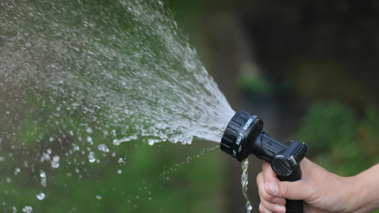 A hand holding a garden hose nozzle spraying water