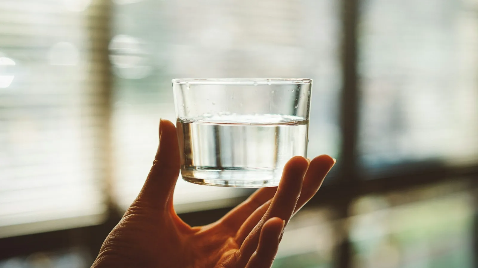 A hand holding a glass of water in soft light