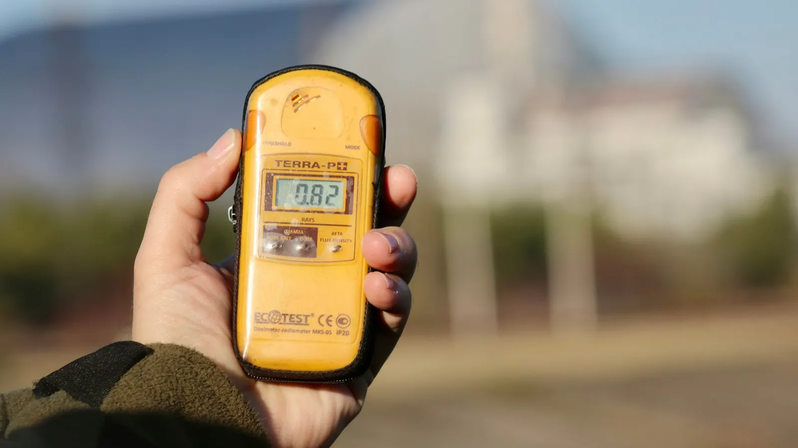A hand holding a yellow radiation counter outdoors