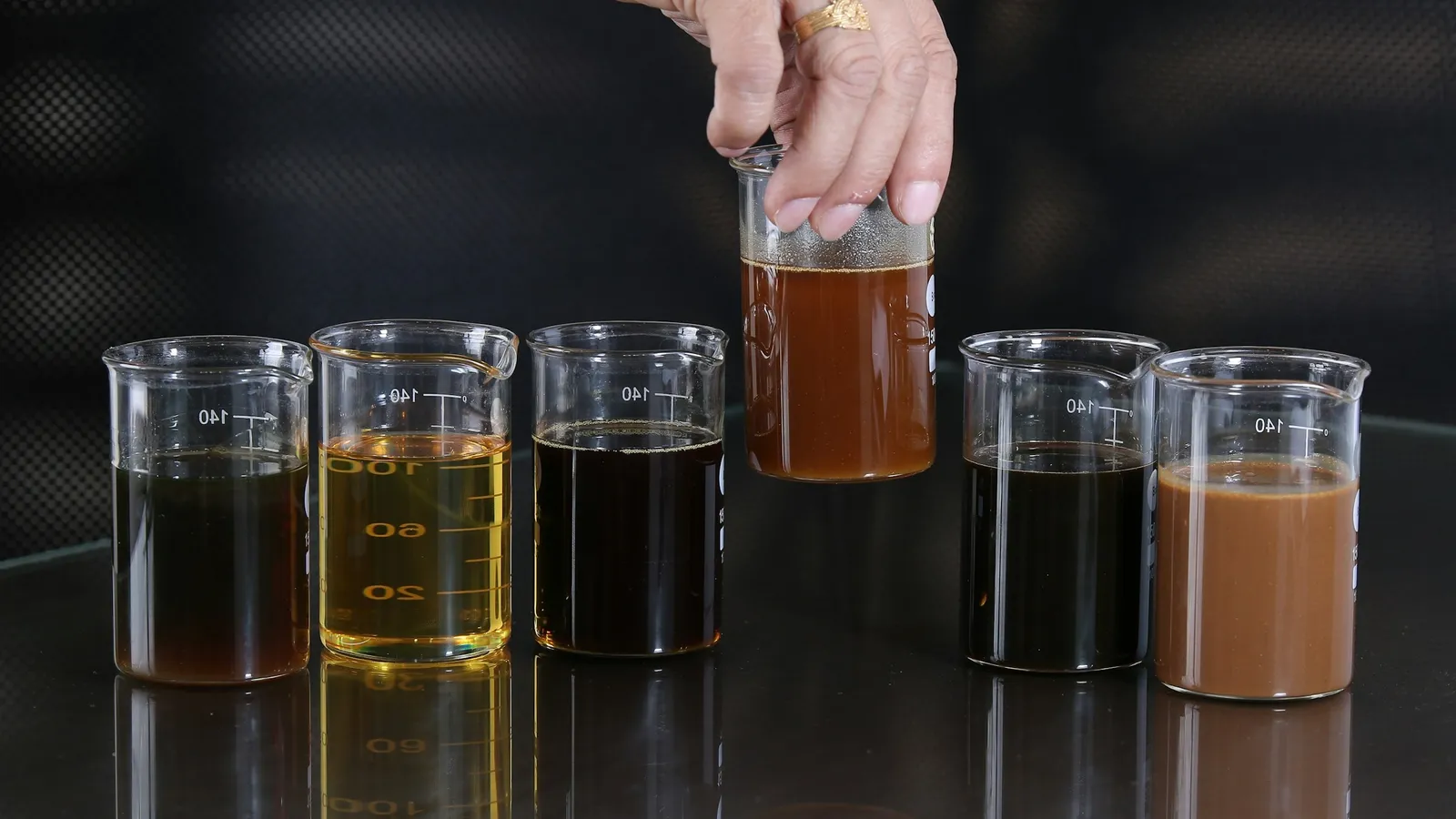 A hand lifting one of several beakers of coloured liquid