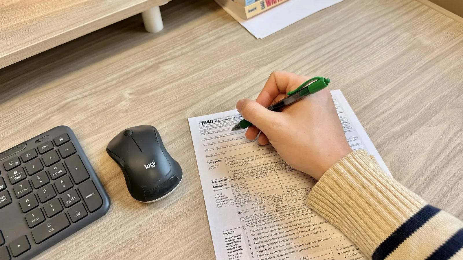A hand marking a printed paper beside a keyboard and mouse