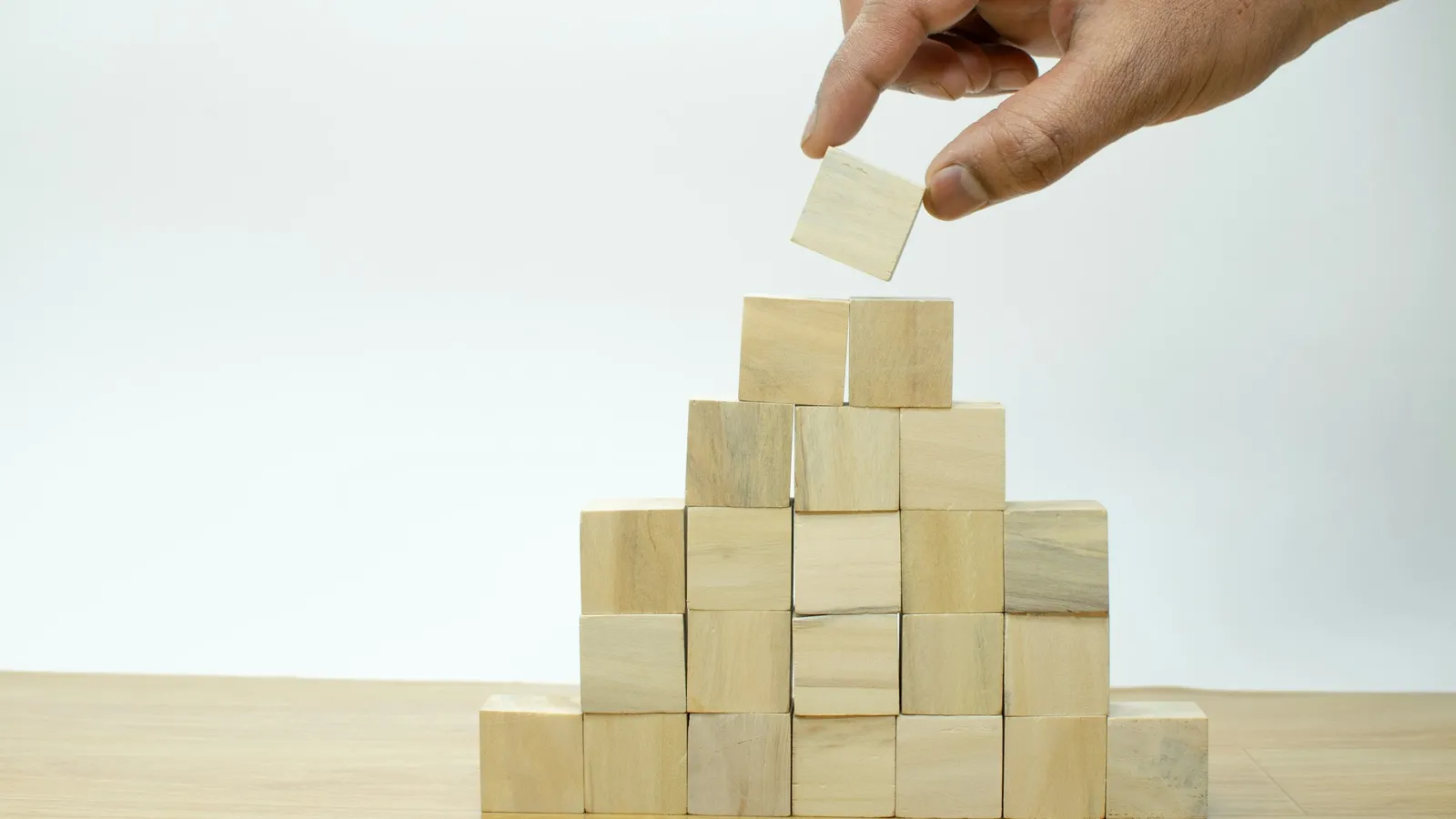 A hand placing a wooden block on top of a stepped pyramid of blocks