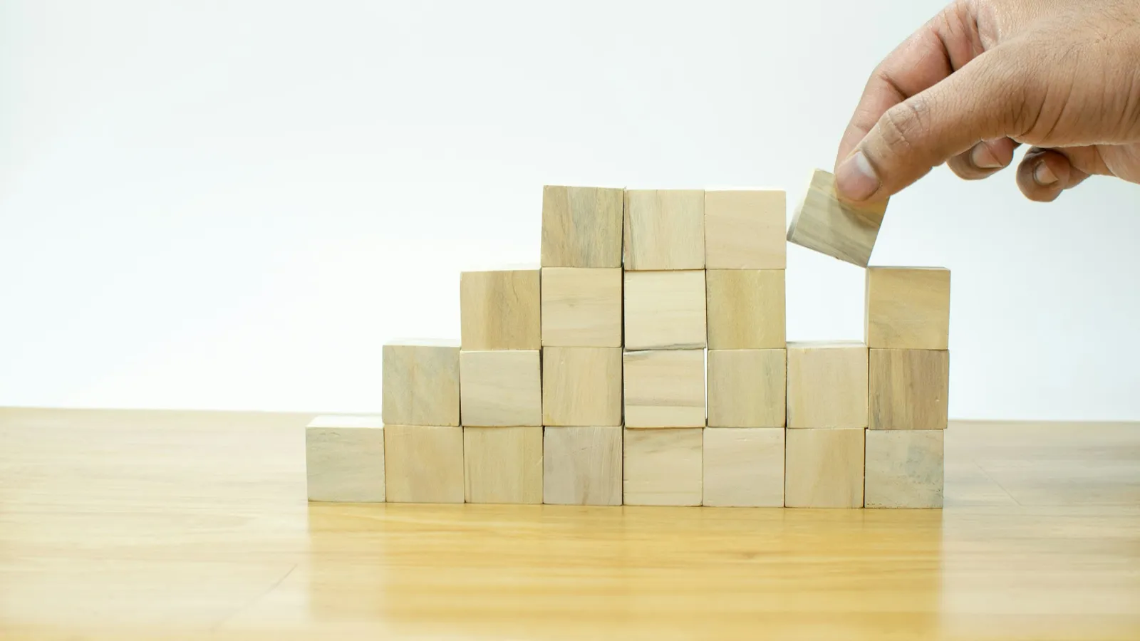 A hand stacking wooden blocks into a pyramid