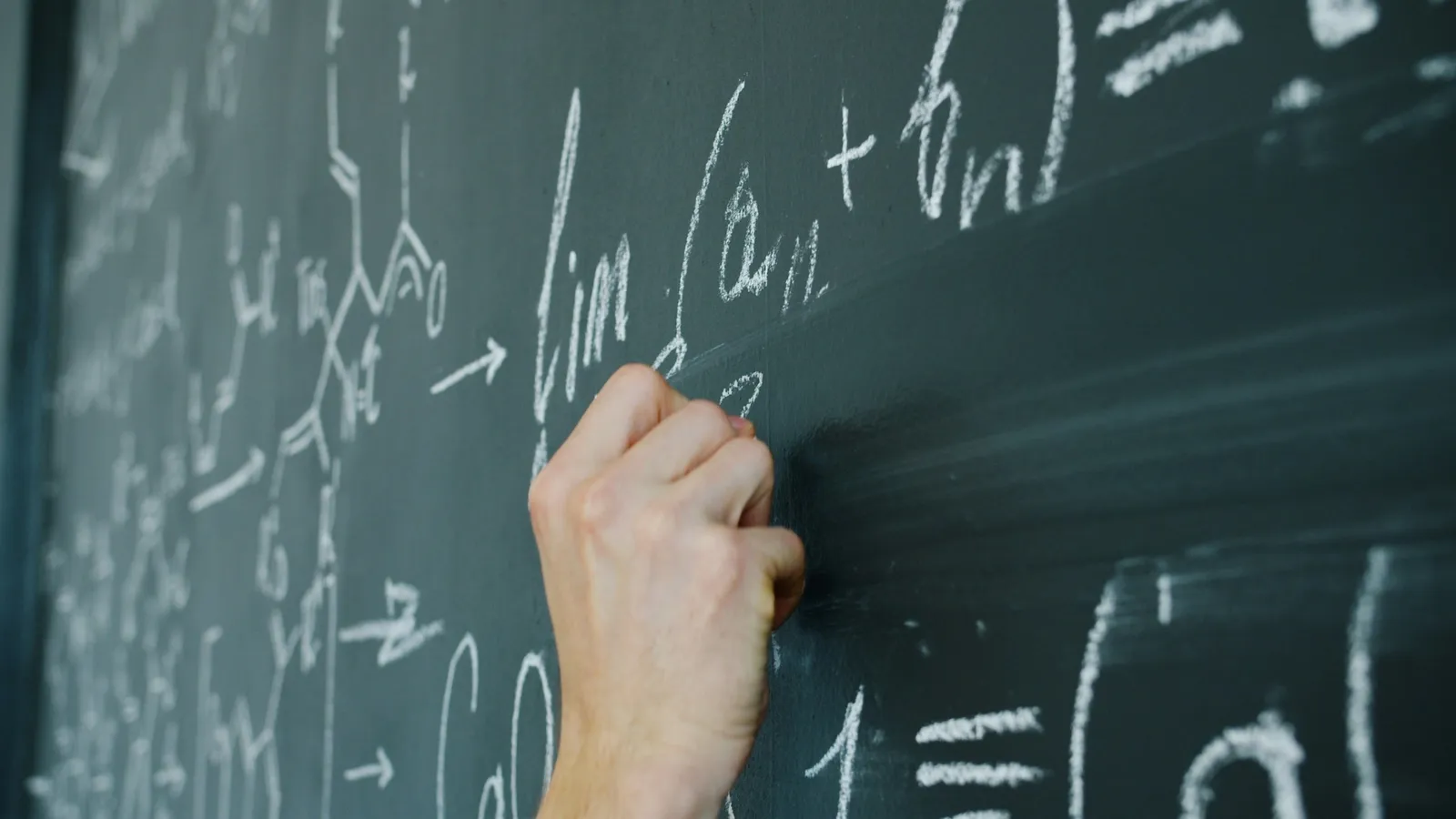 A hand writing calculus formulas in chalk on a green board