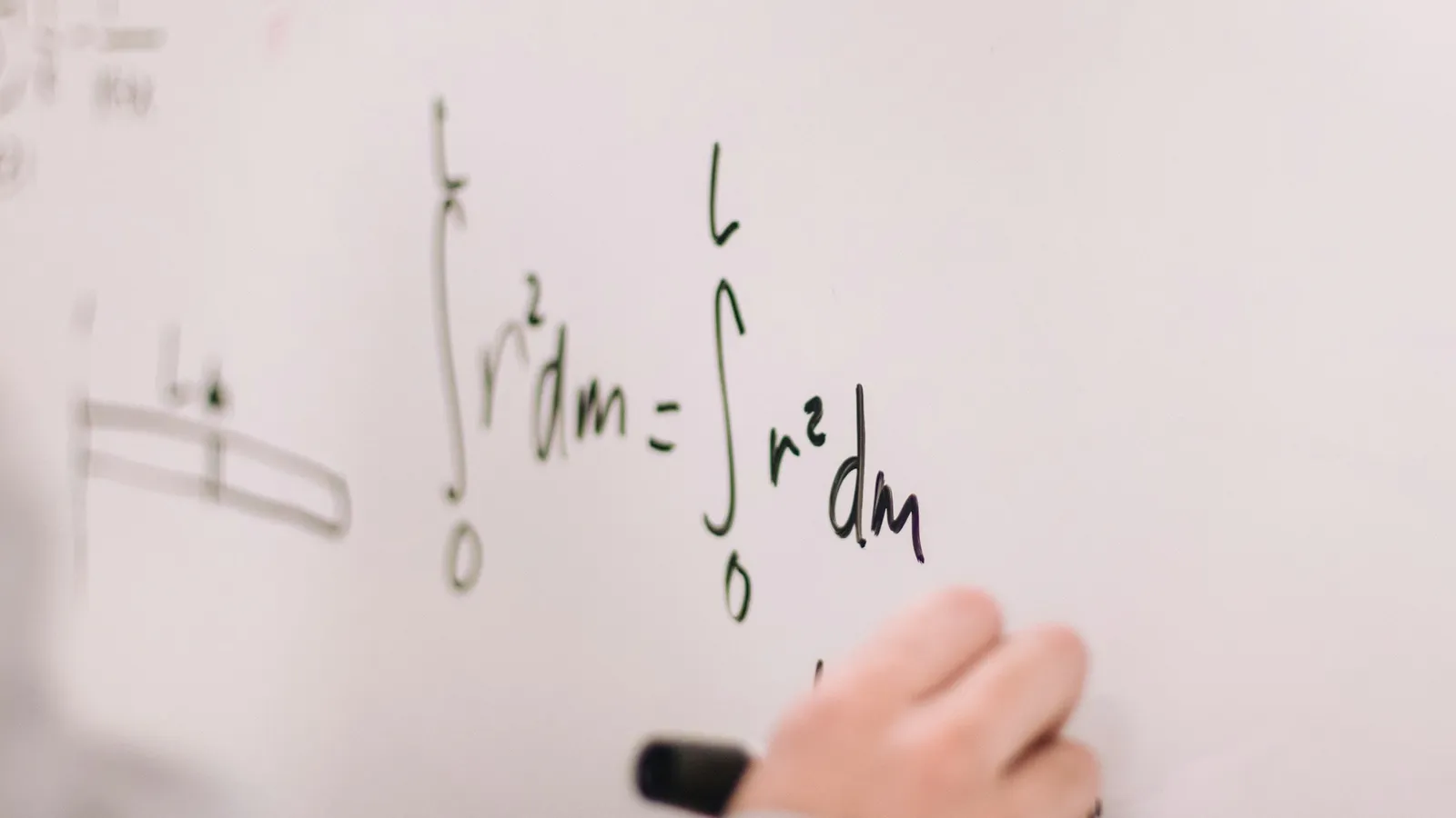 A hand writing equations on a whiteboard with a black marker
