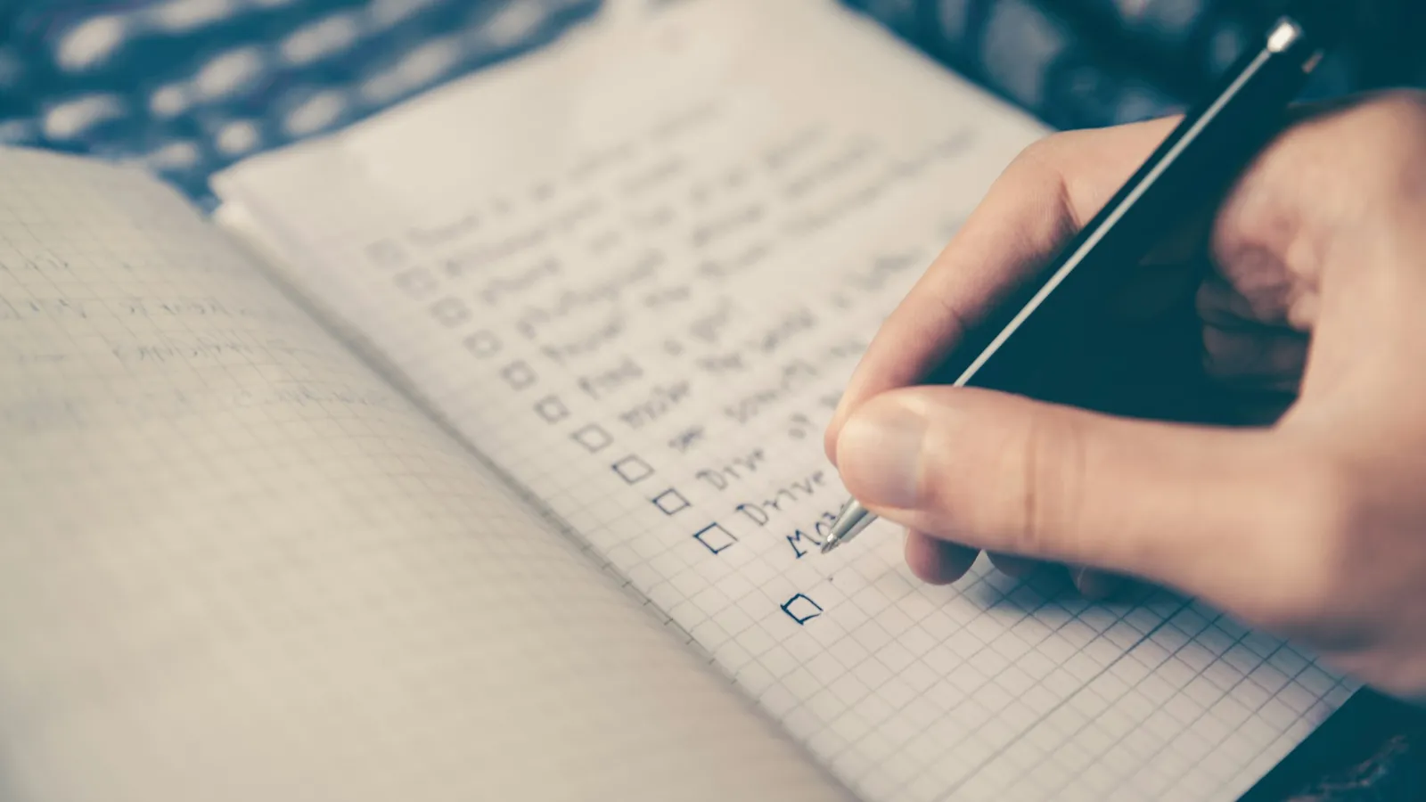 A hand writing in a lined notebook with a pen