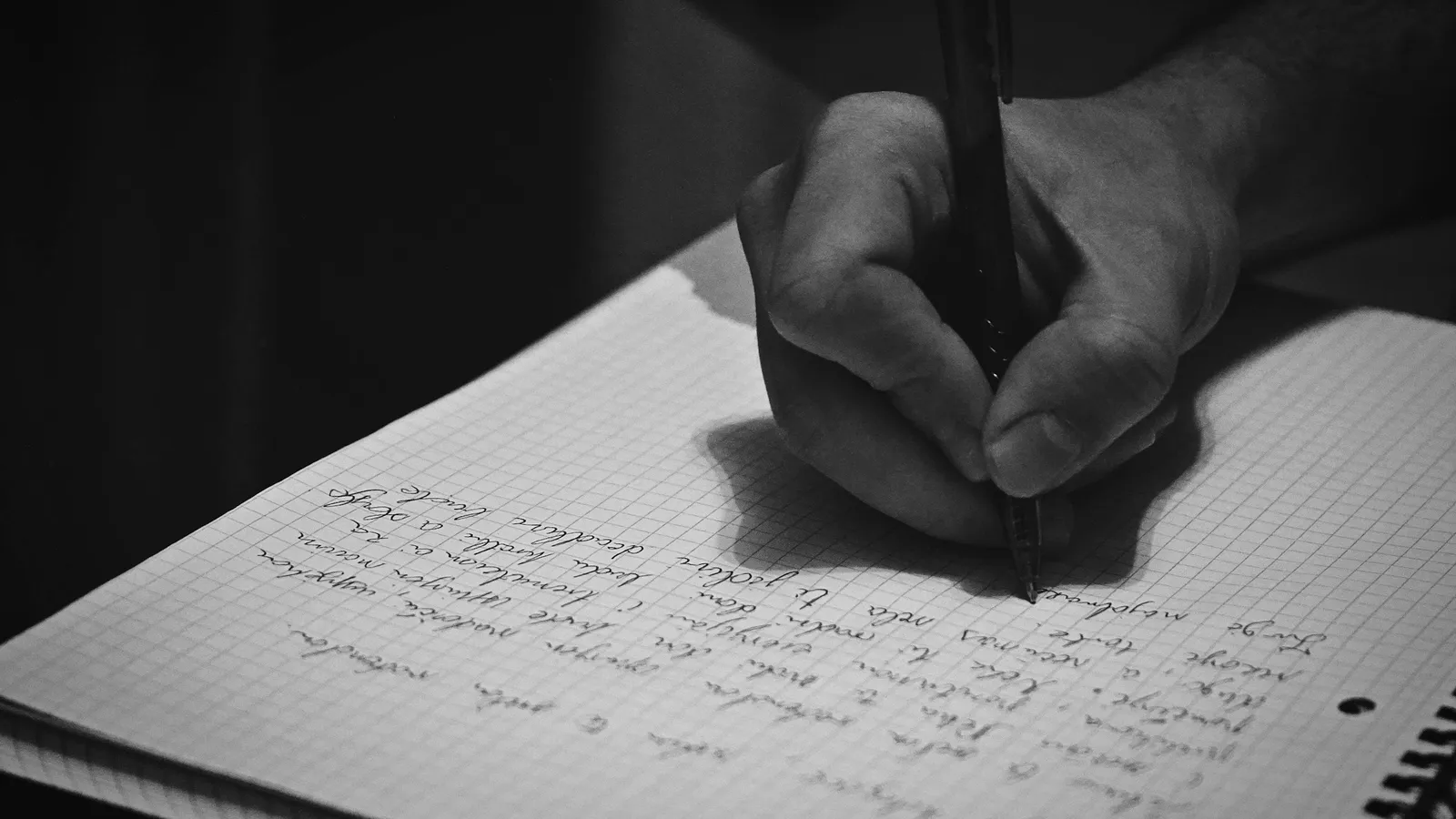 A hand writing in a notebook with a pen, in black and white