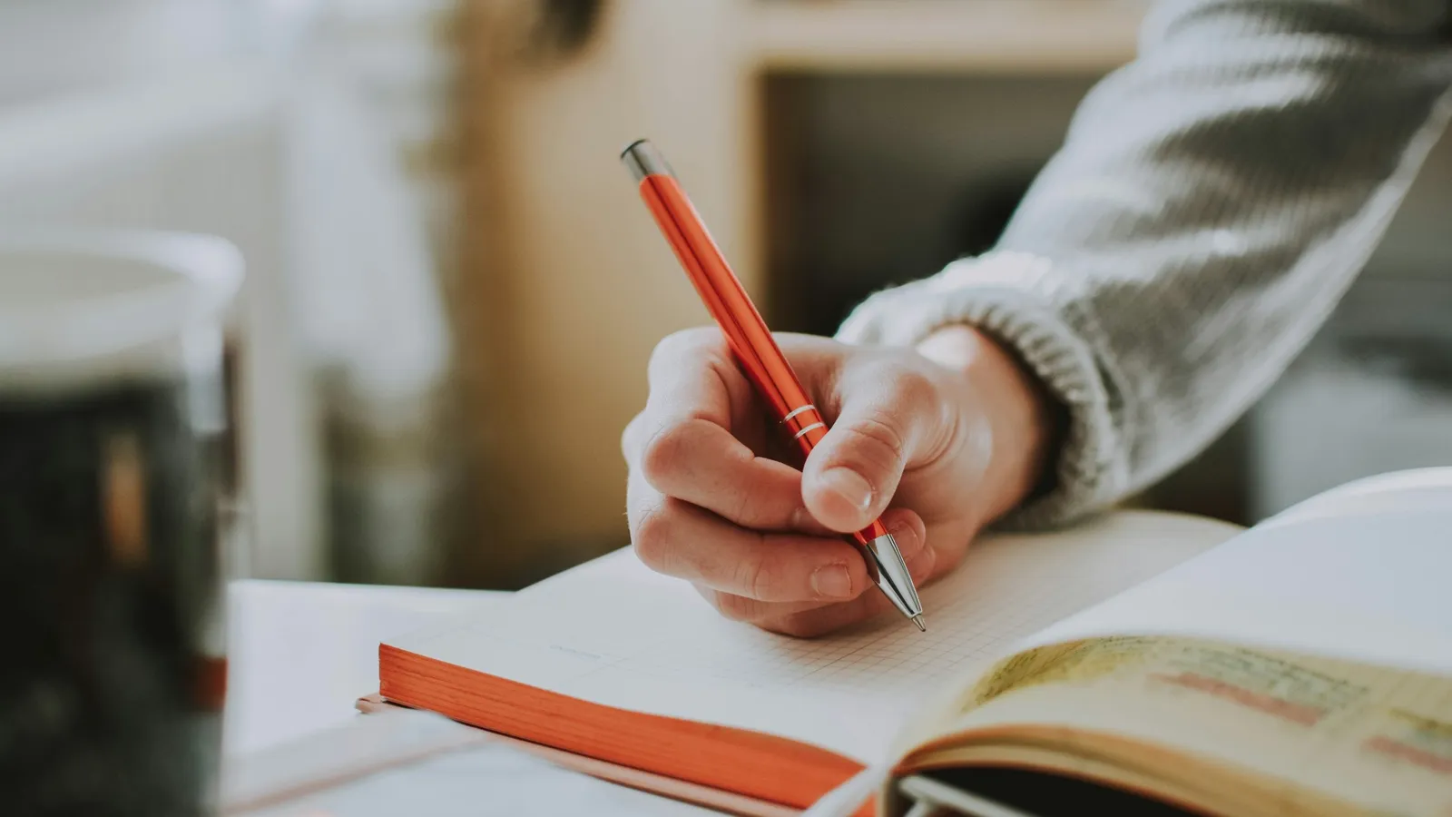A hand writing in a notebook with a red pen