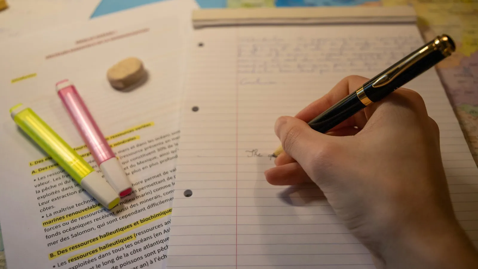 A hand writing notes with a pen beside highlighters